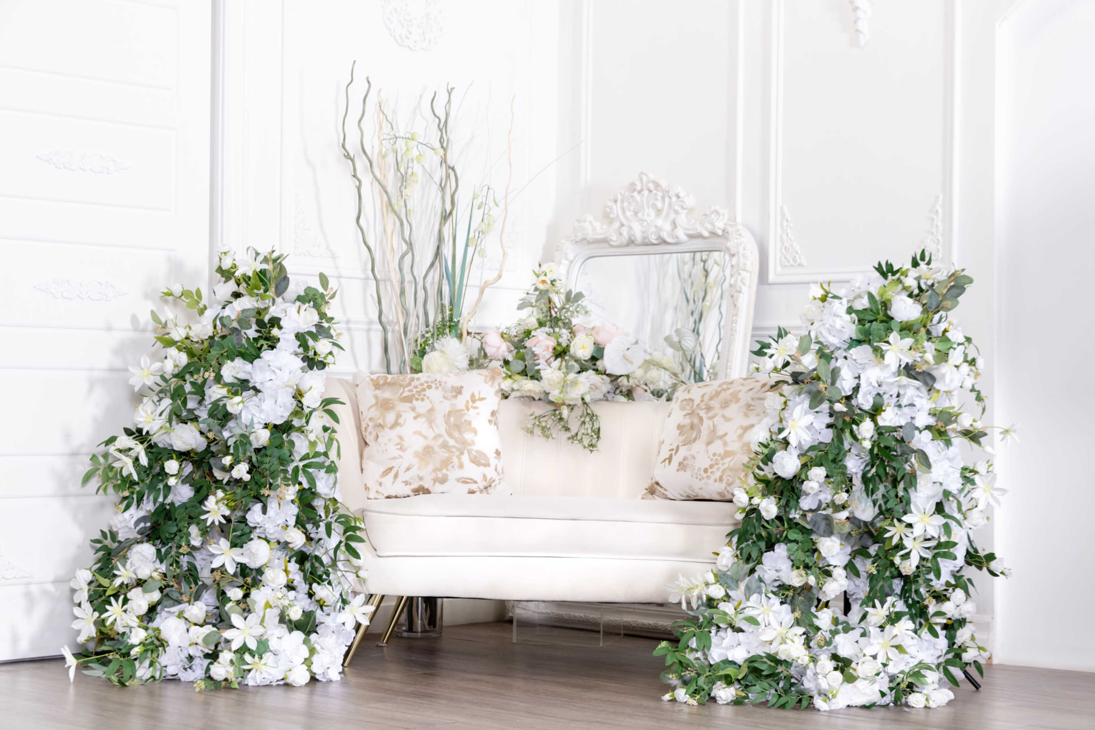 A white sofa adorned with floral arrangements on either side is positioned against a bright, decorative wall.