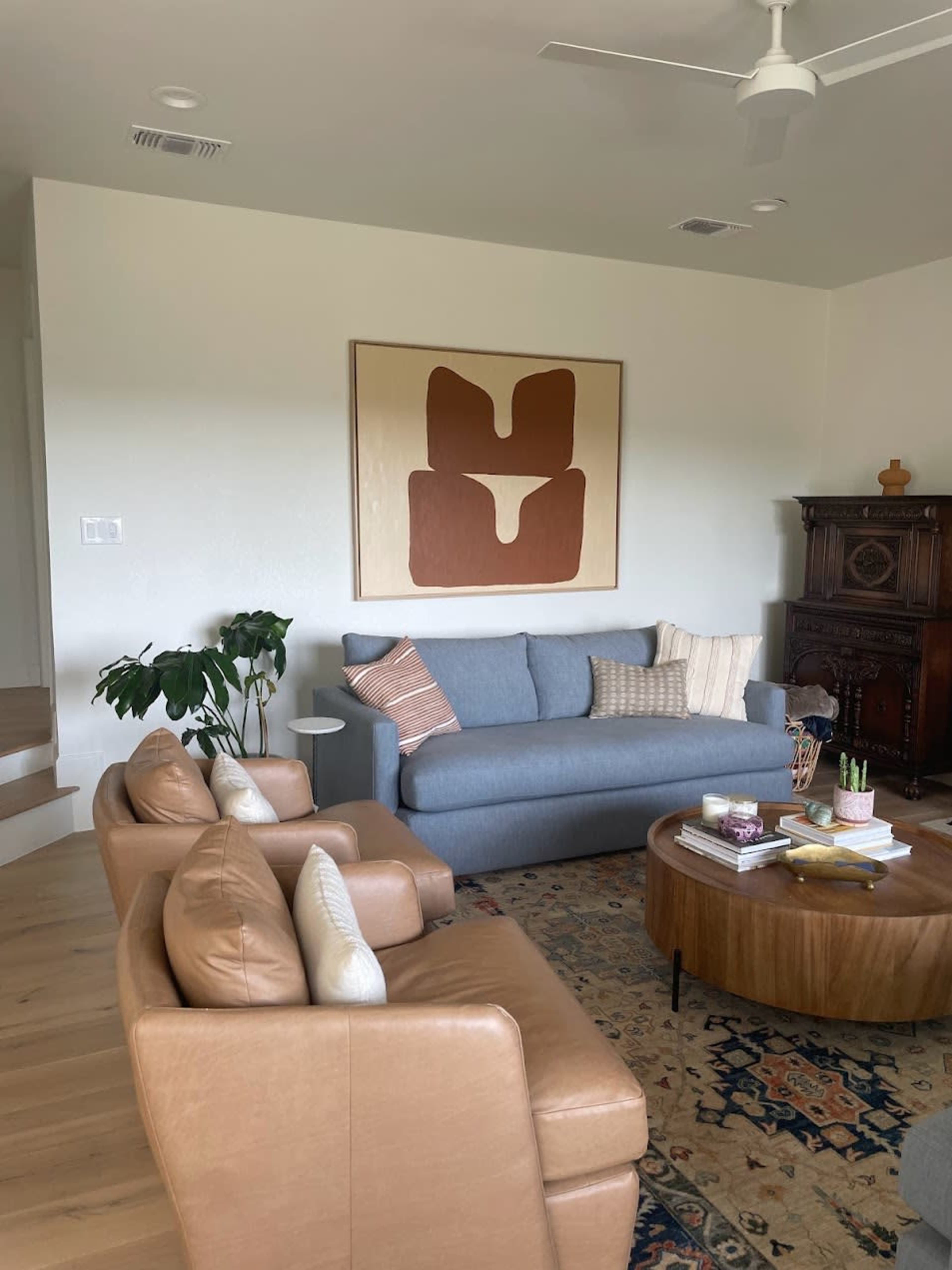 The living room features a blue sofa, two tan leather chairs, a round coffee table, and an abstract wall art piece above the sofa.