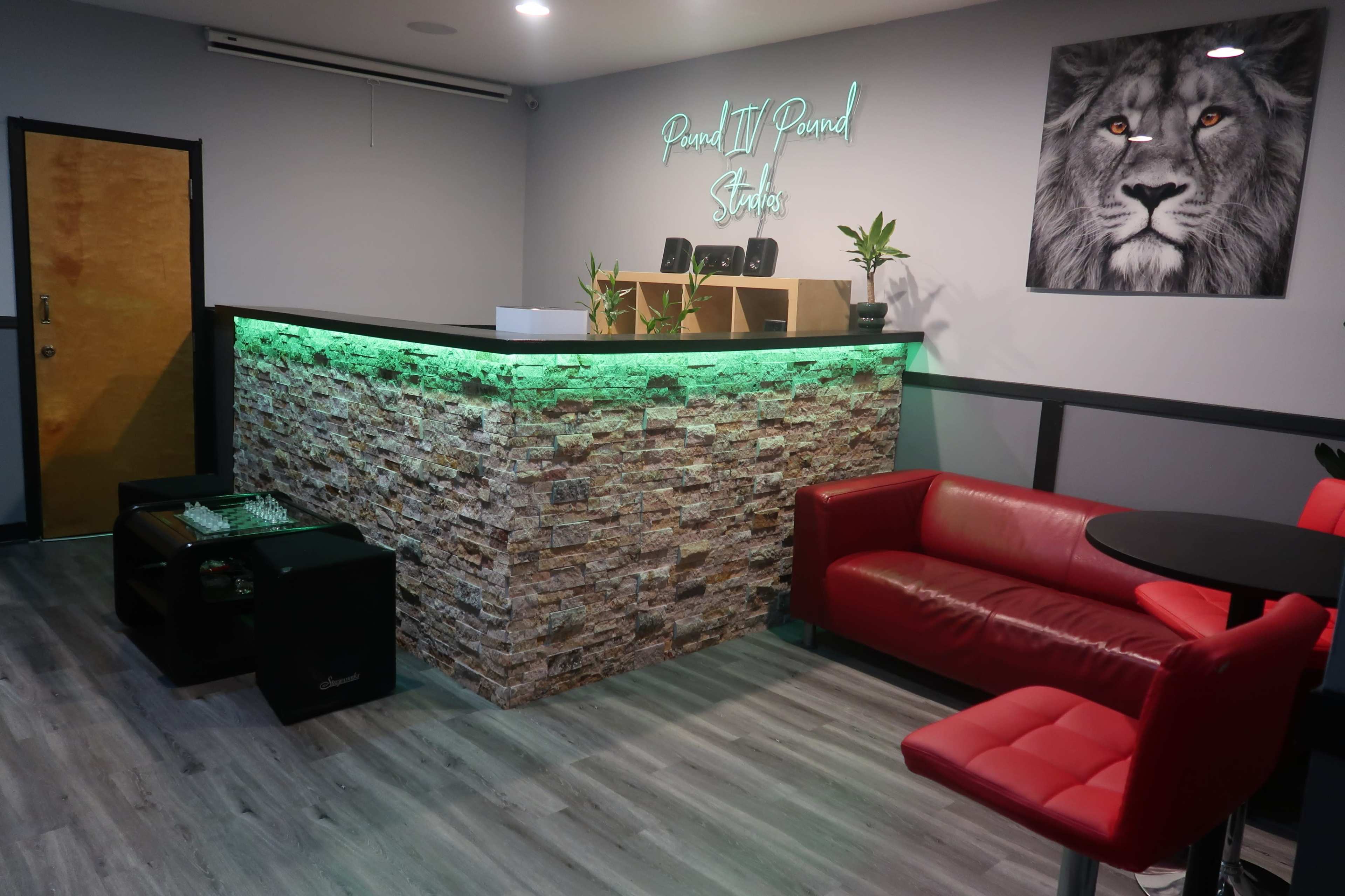 The image depicts a modern studio reception area with a stone-patterned front desk illuminated by green lights, furnished with a red sofa and a black table.