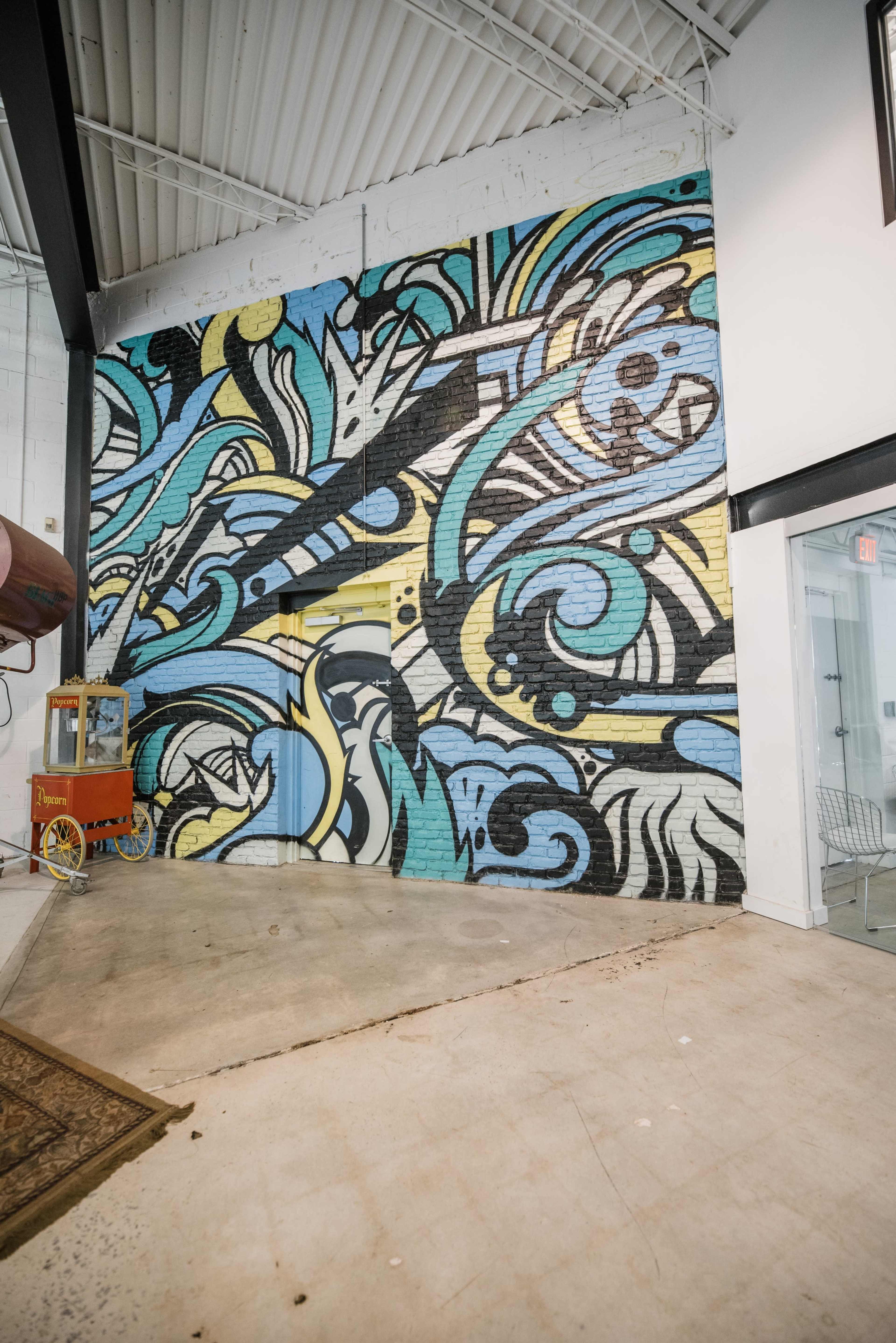 A colorful mural featuring abstract swirls and shapes covers a brick wall in a spacious interior.