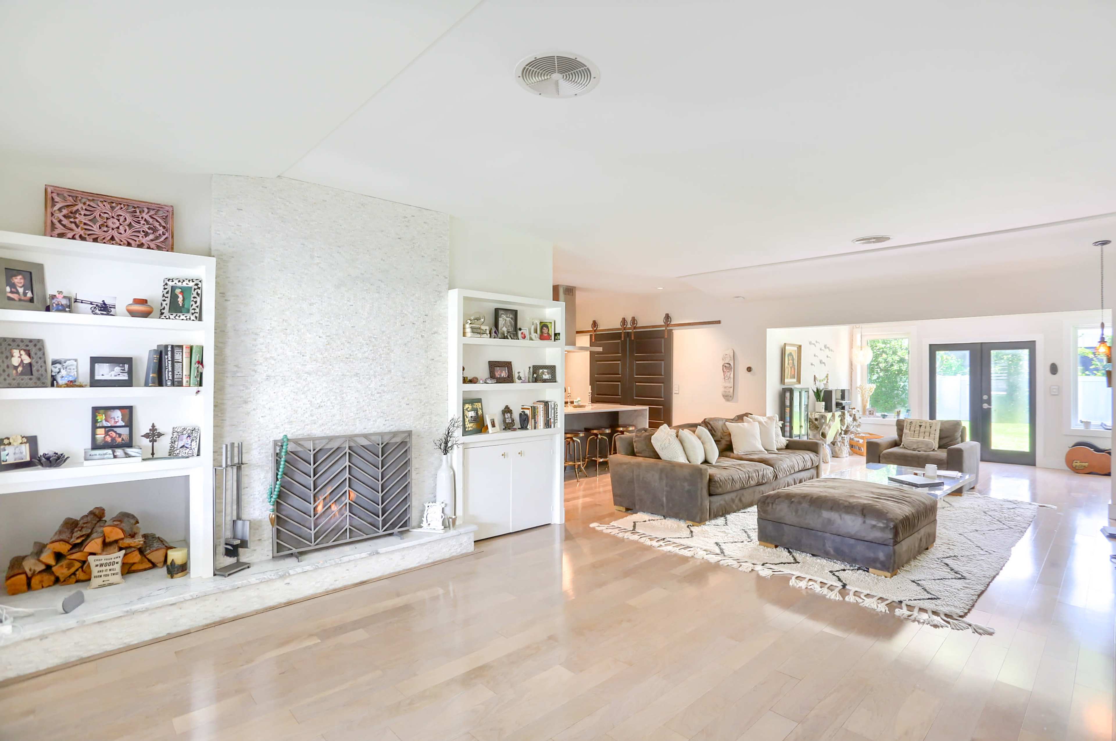 A spacious living room featuring a modern fireplace, built-in shelves with decorative items, and a large sectional sofa arranged on a light-colored area rug.