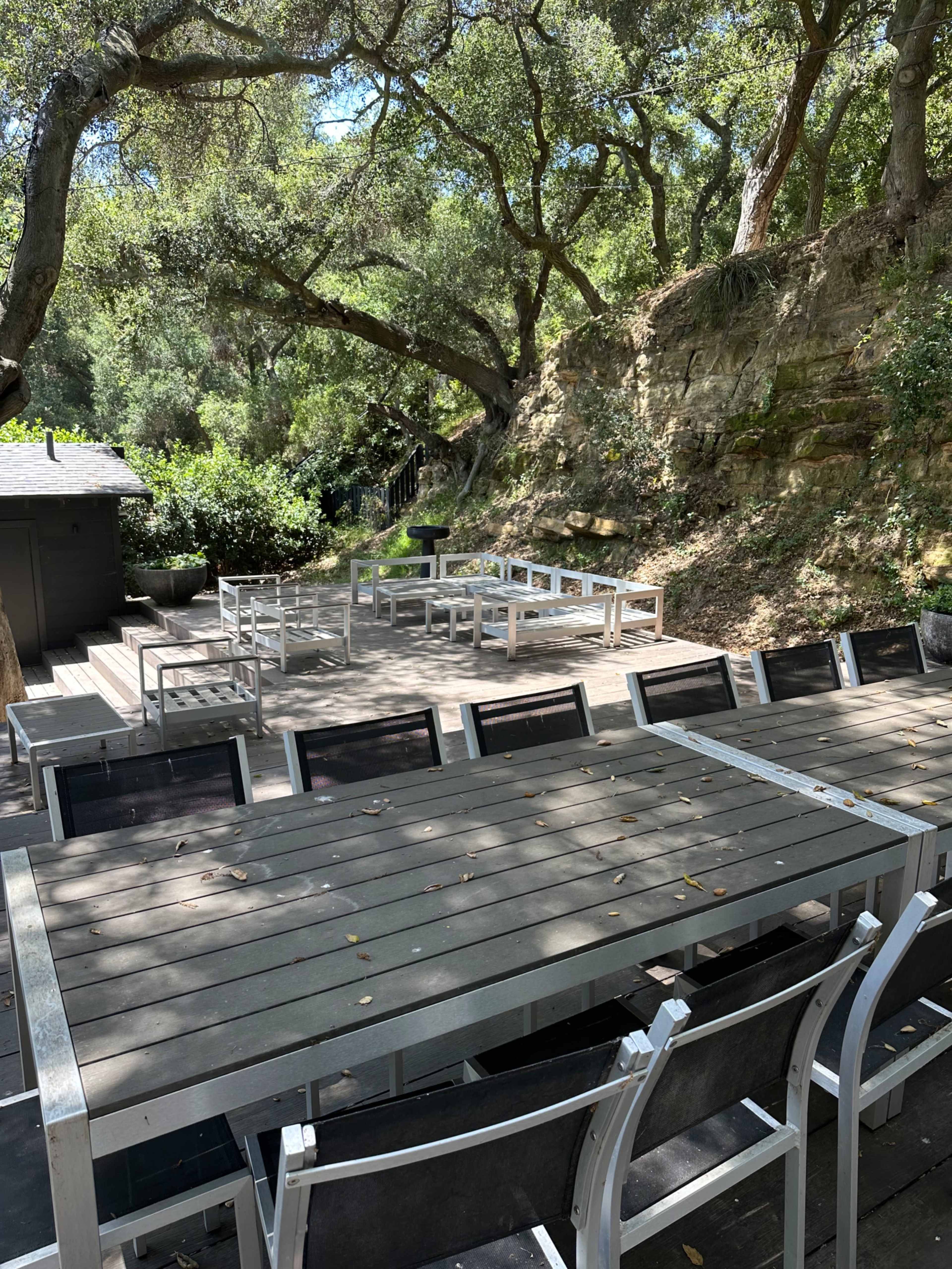 A spacious outdoor dining area with metal tables and chairs is surrounded by trees and rocky terrain.
