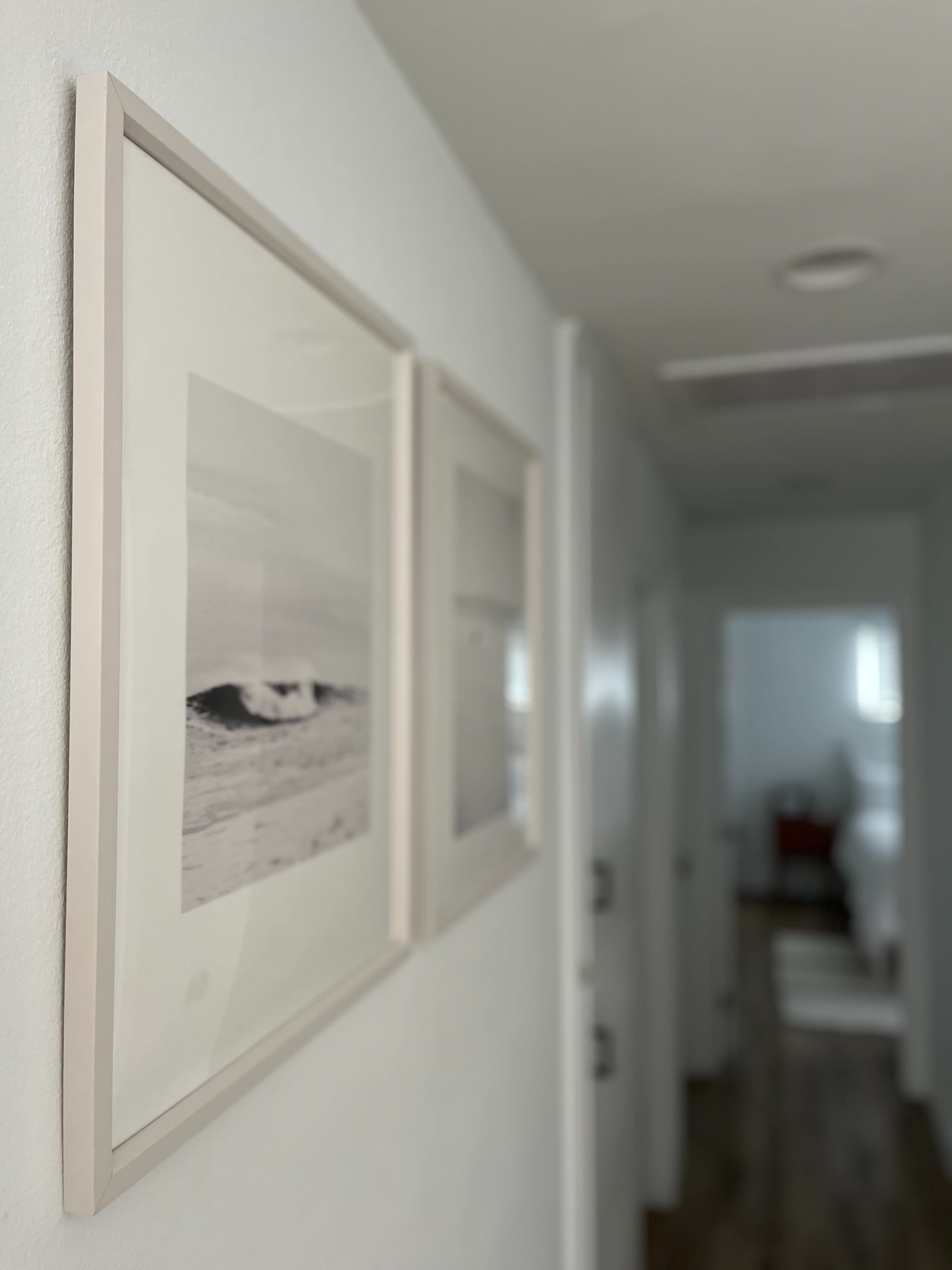 Two framed black-and-white photographs of waves displayed on a white wall in a hallway.