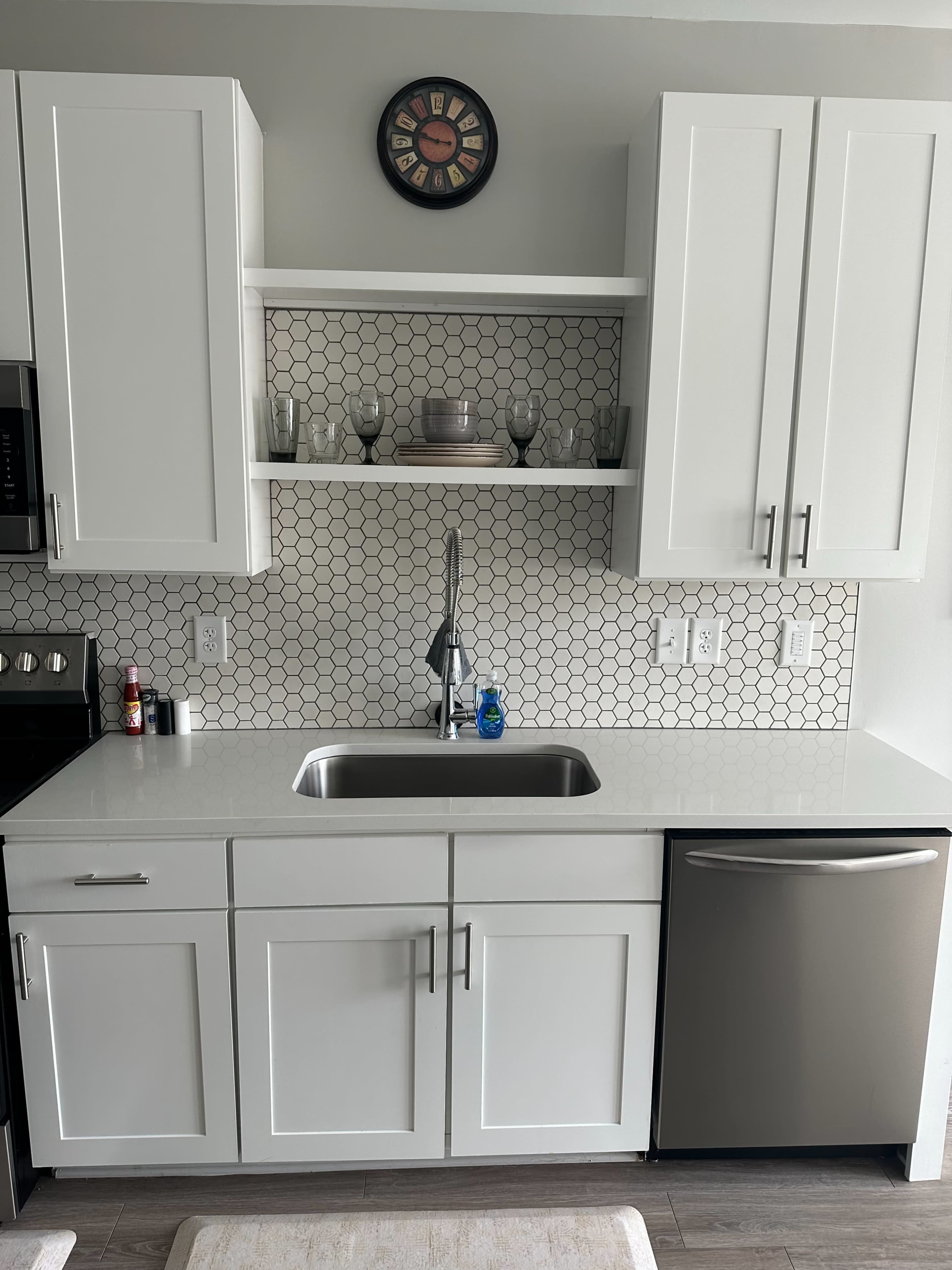 A modern kitchen with white cabinetry, a stainless steel sink, and a backsplash featuring hexagonal tiles.