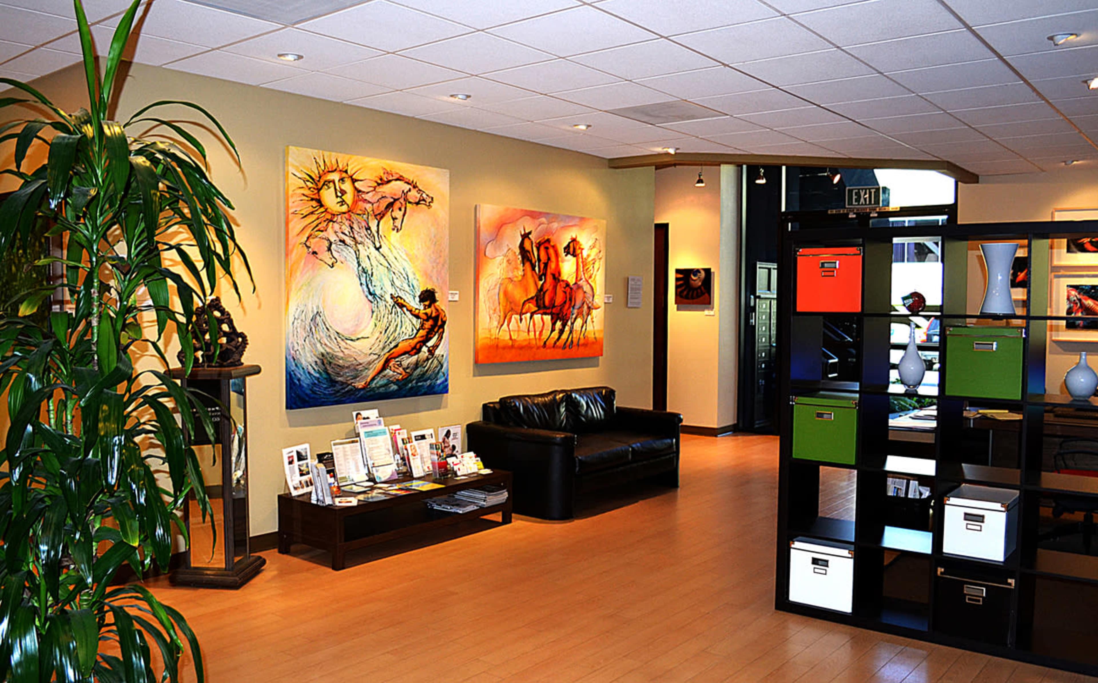 A modern art gallery featuring vibrant paintings on the walls, a black leather couch, and a shelving unit with colorful storage boxes.