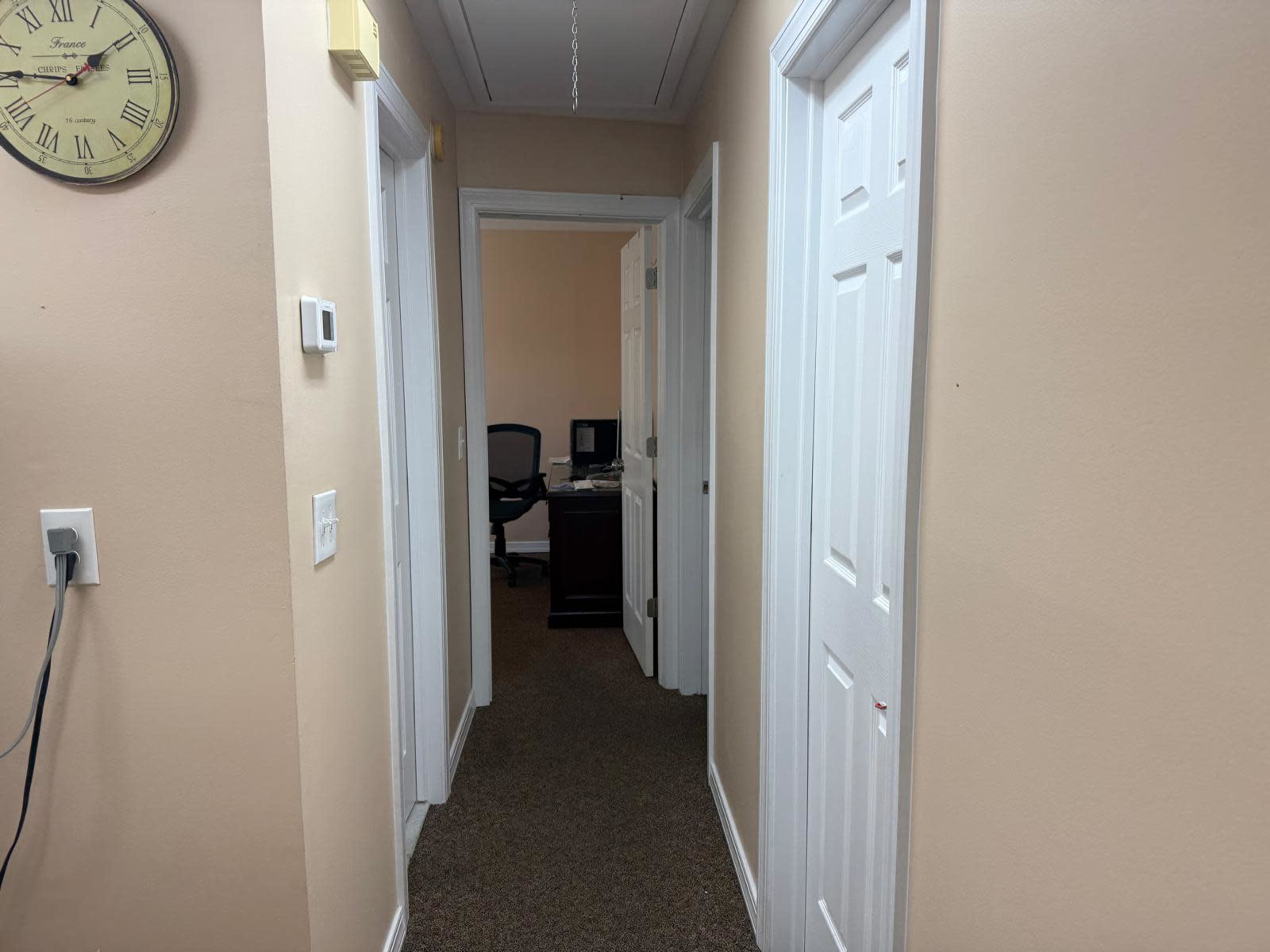 A hallway with two closed doors on the right and a visible desk with a chair at the far end.