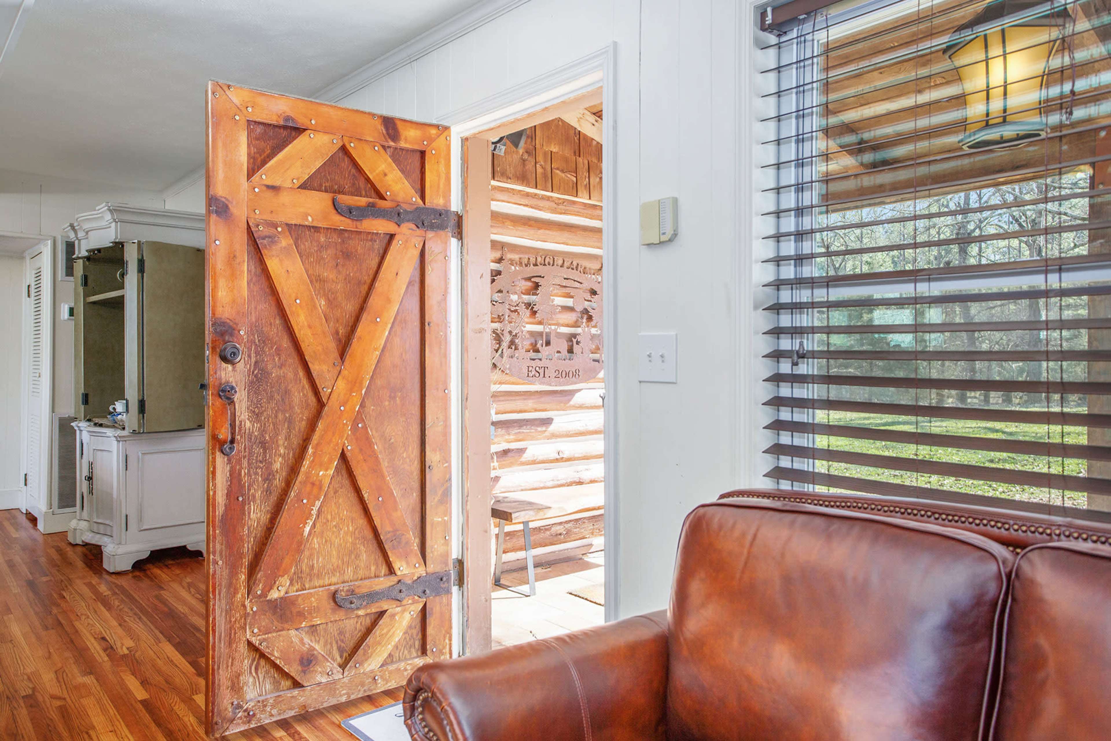 A wooden door is partially open, revealing a rustic interior and an outdoor view through a window with blinds.