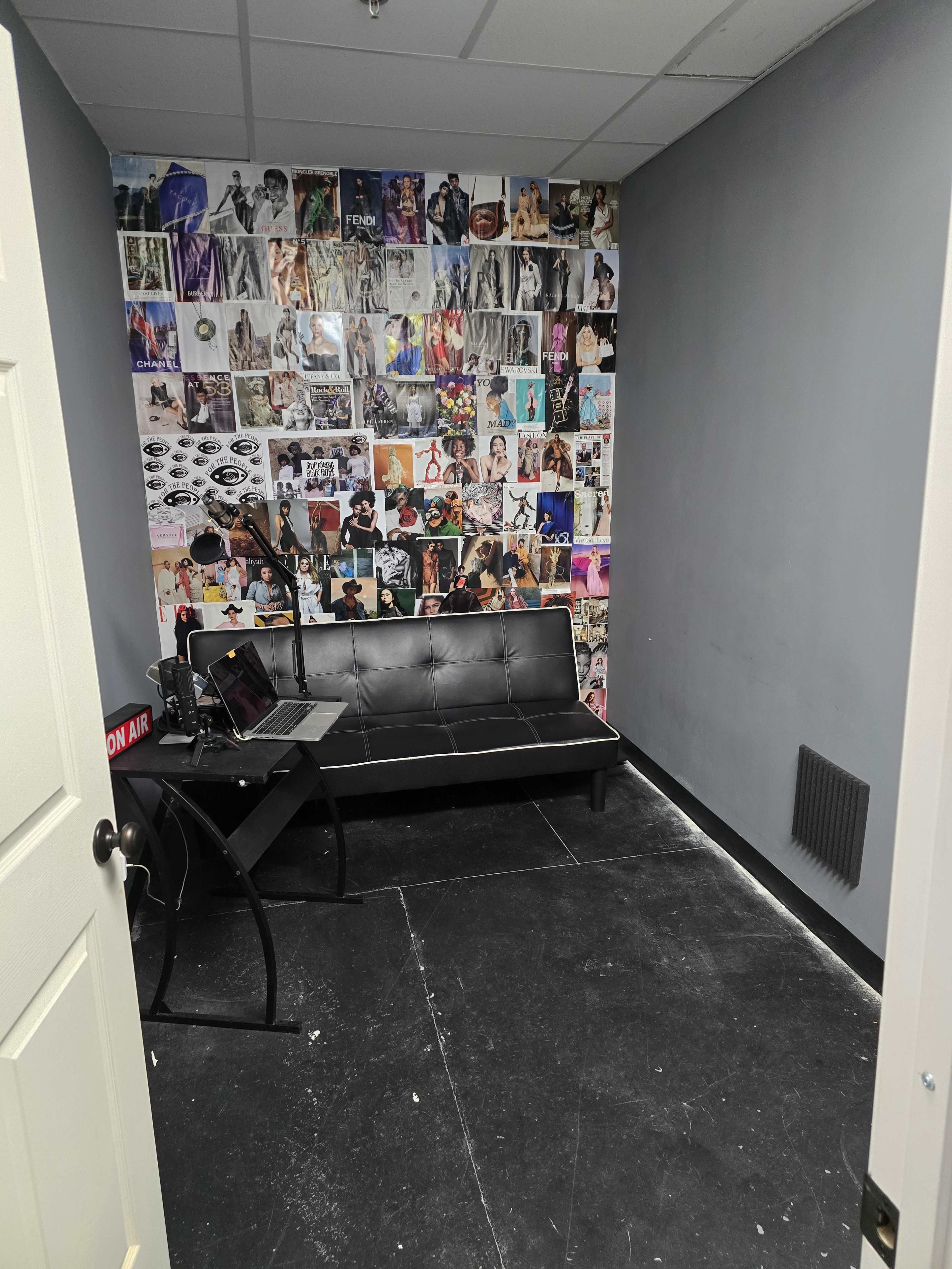 A small room with a black futon, a desk with a laptop, and a wall covered in various photographs.