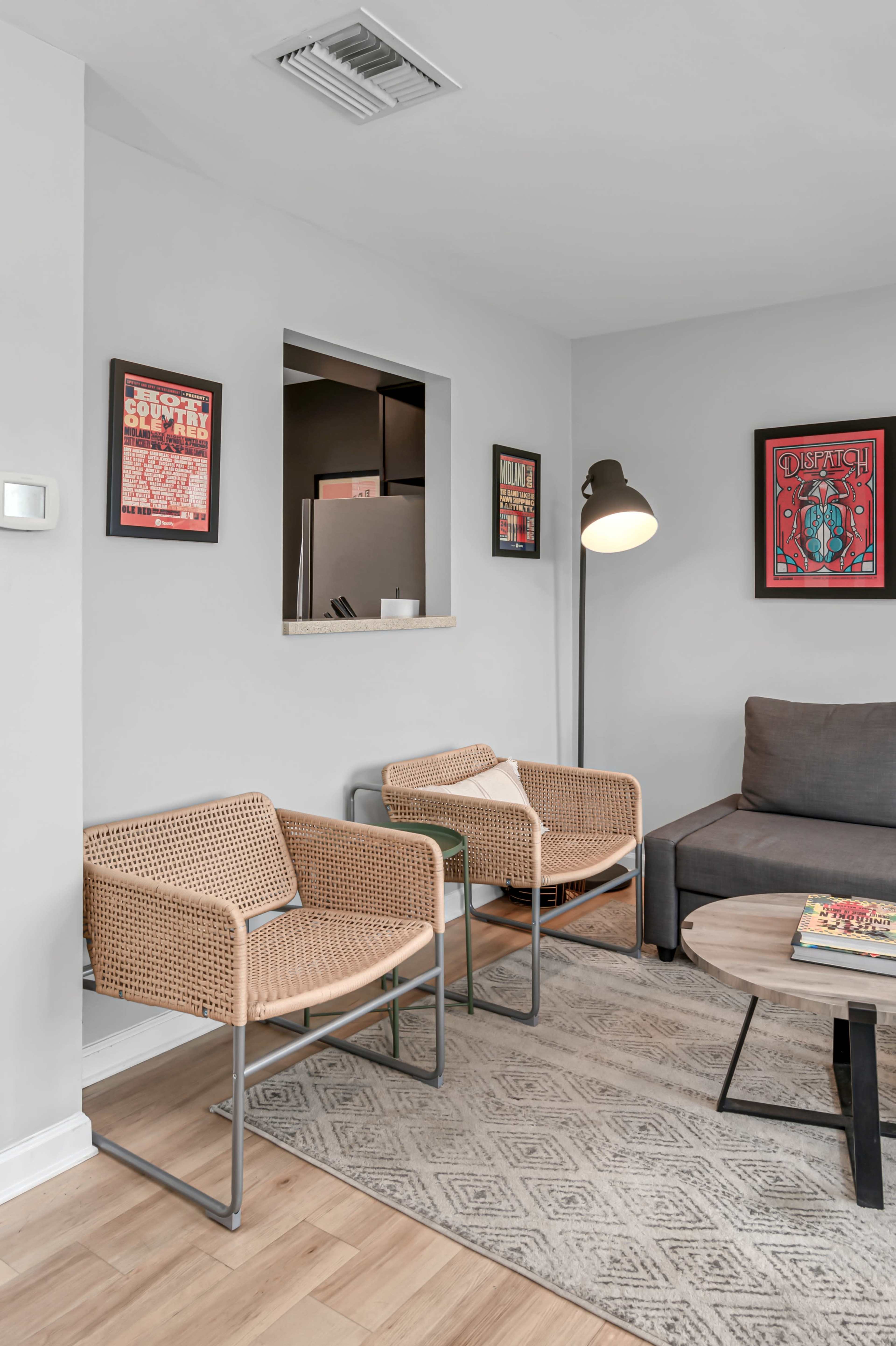 A modern living room featuring two woven chairs, a gray sofa, a floor lamp, and framed artwork on the walls.