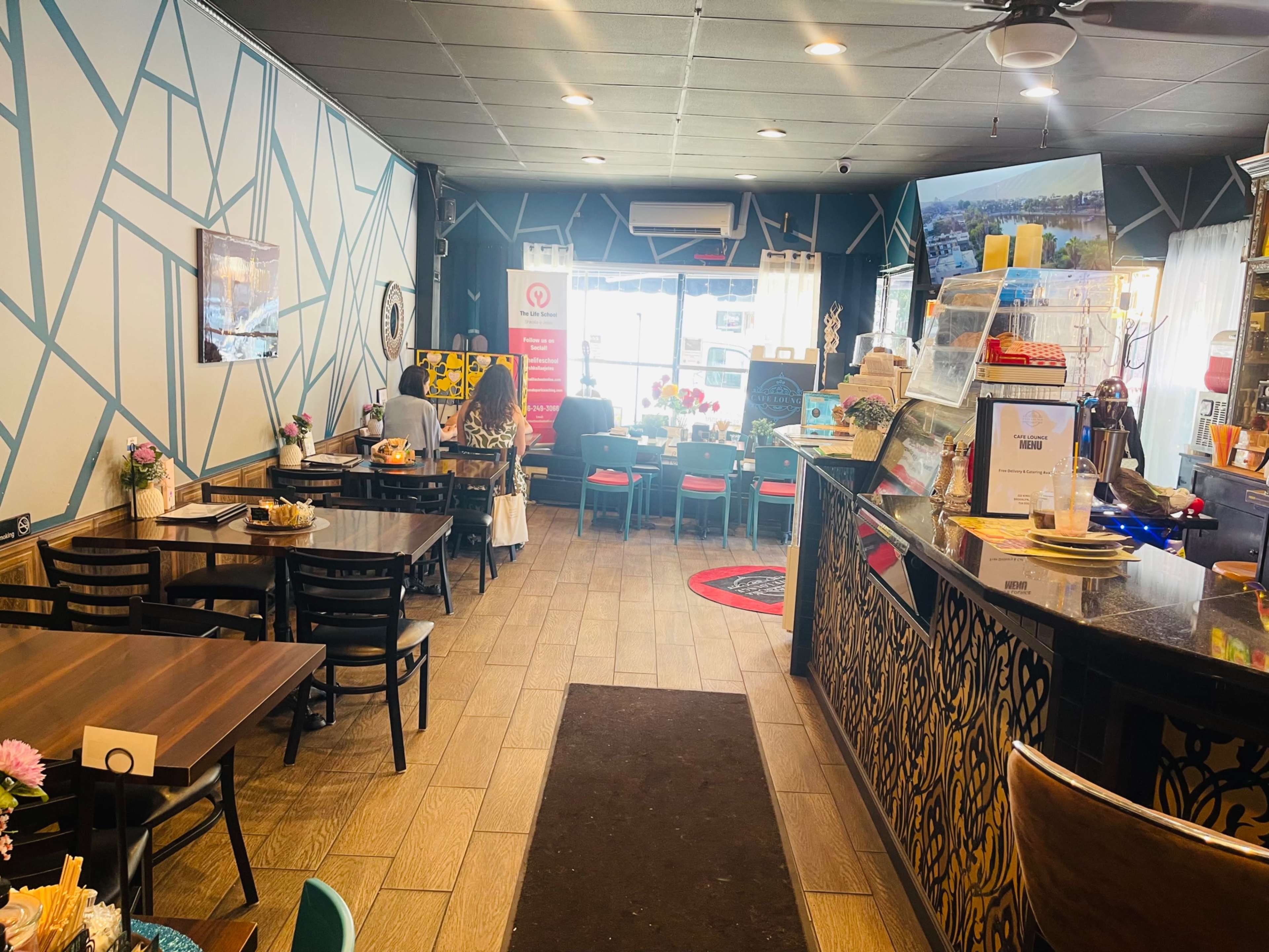 The image shows the interior of a cafe with tables and chairs arranged on the left side, a counter with decorative elements on the right, and patrons seated in the background.