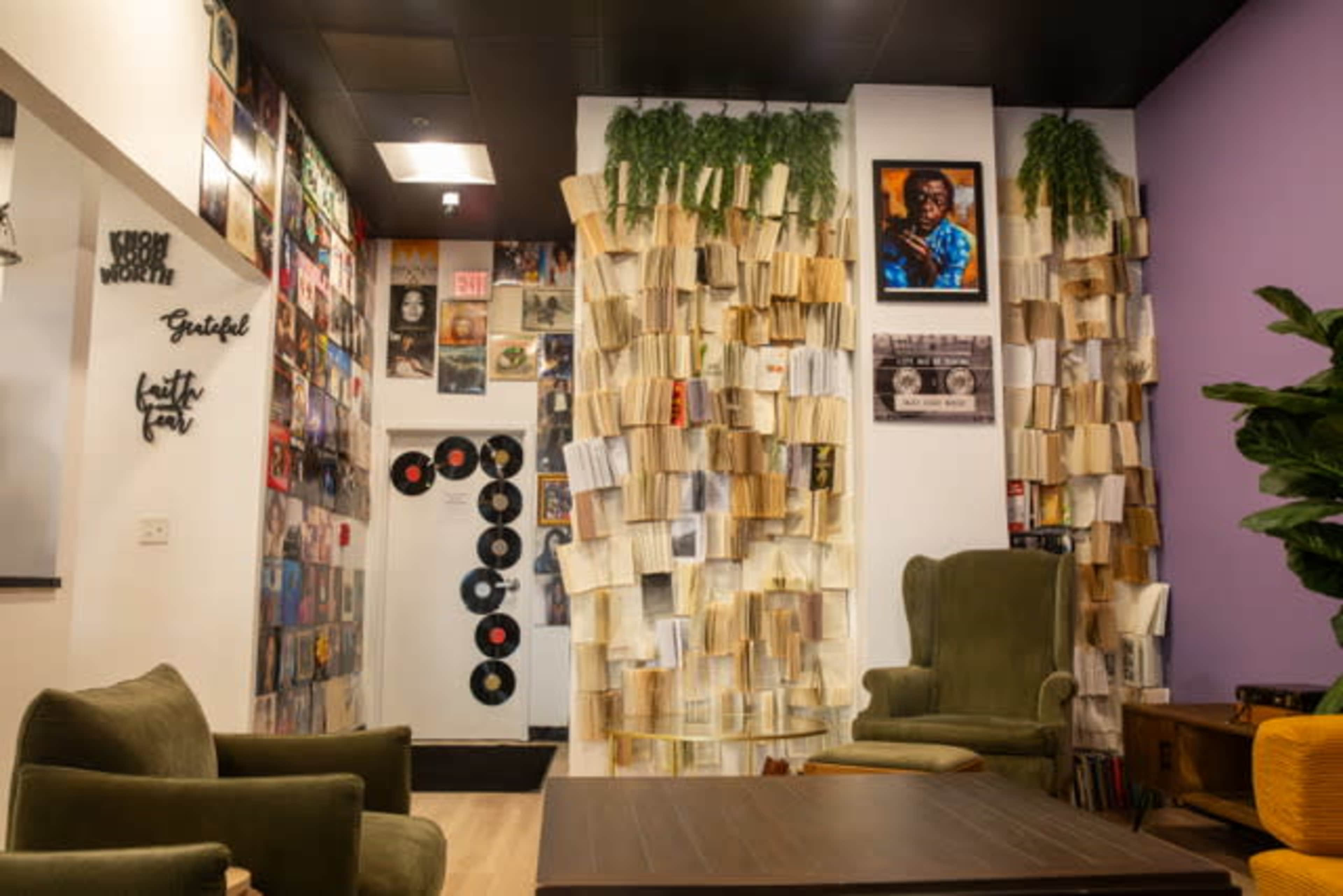 The image shows a cozy room decorated with bookshelves filled with records, framed pictures on the walls, and two green armchairs facing a wooden table.