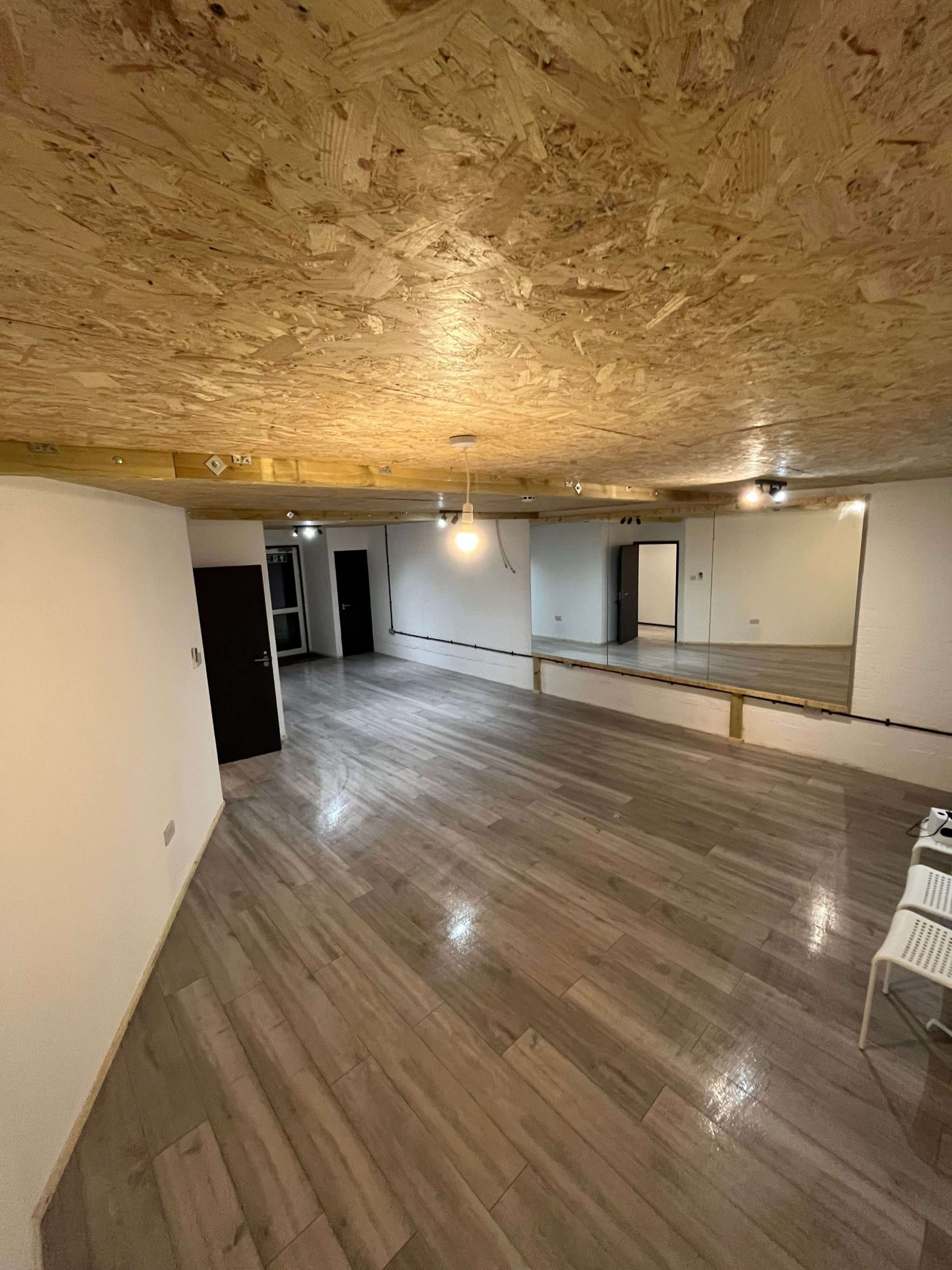 A spacious interior room with a wooden ceiling, wooden floor, and a large mirror along one wall.