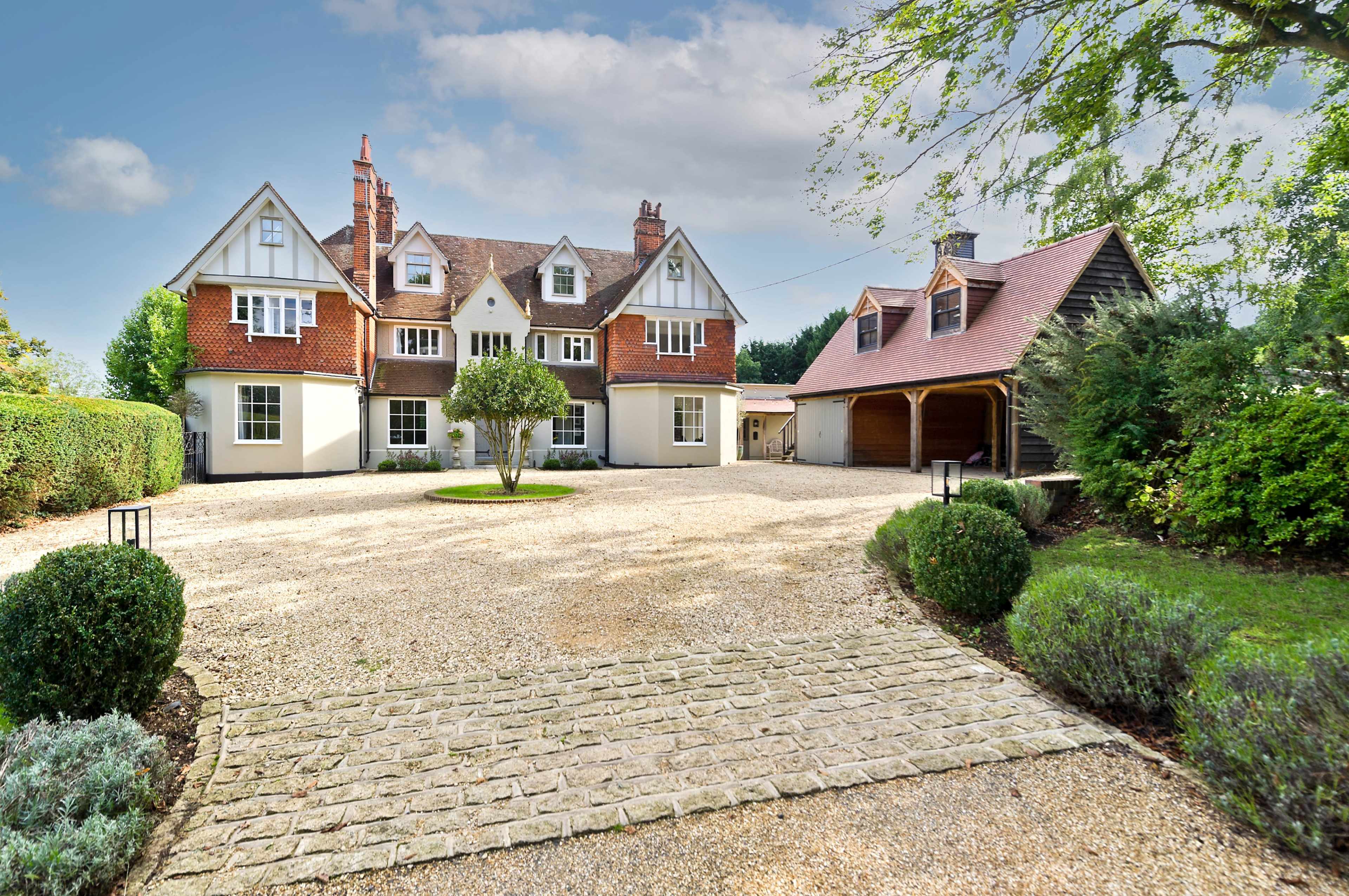 A large, two-story house with a gravel driveway, manicured lawns, and surrounding trees.