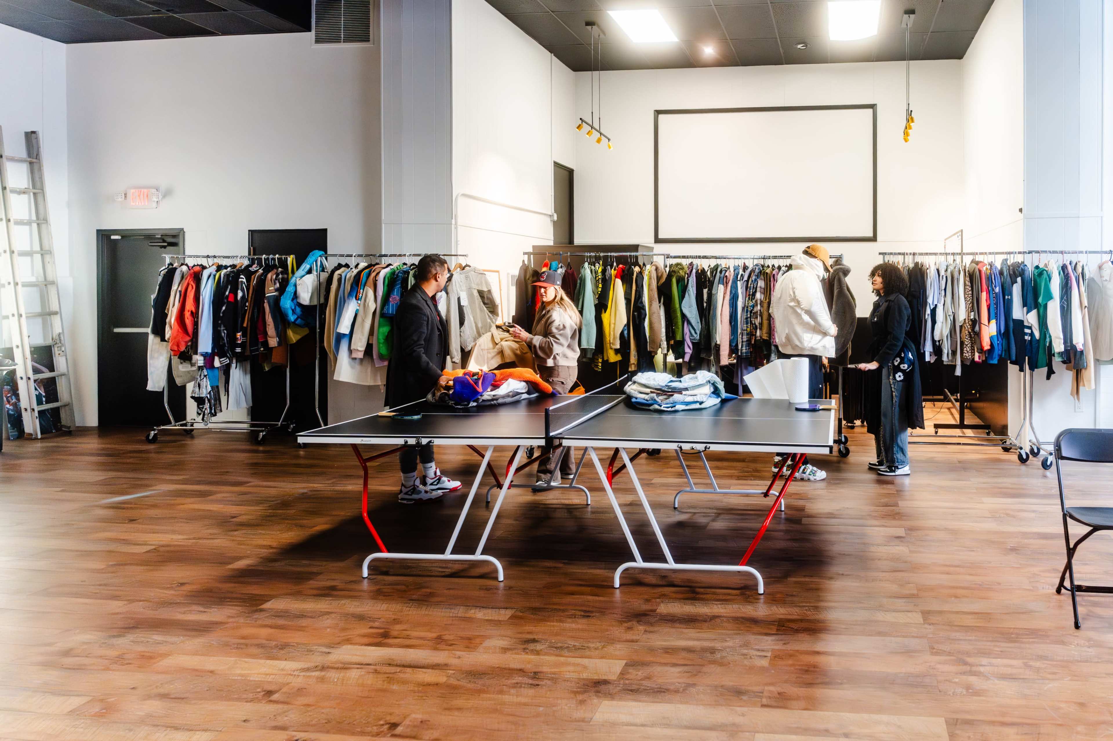 A group of people sorts through clothing displayed on racks in a spacious retail environment with wooden flooring.