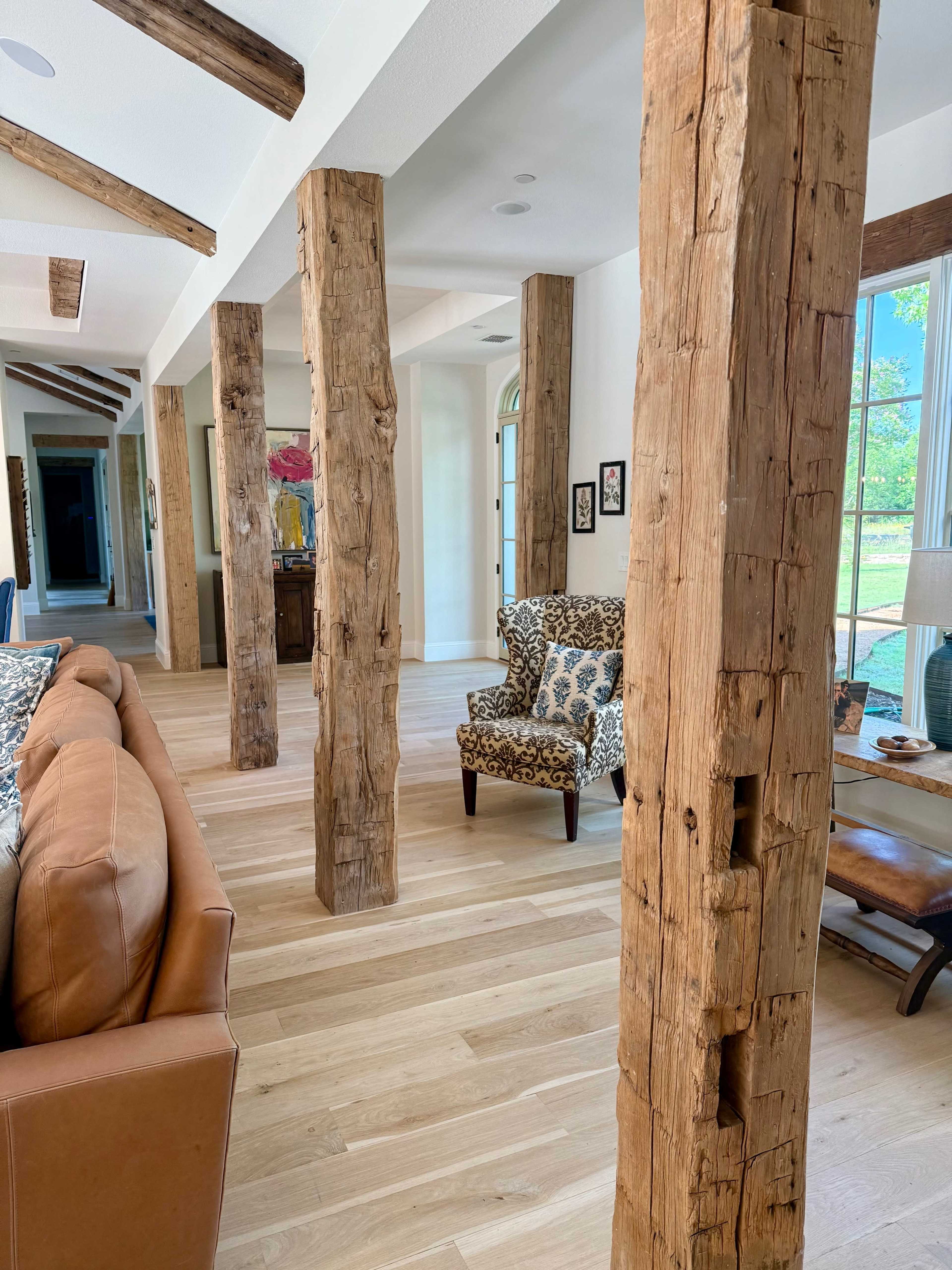 The interior of a modern living space features wooden beams and columns with a leather sofa and a patterned chair.