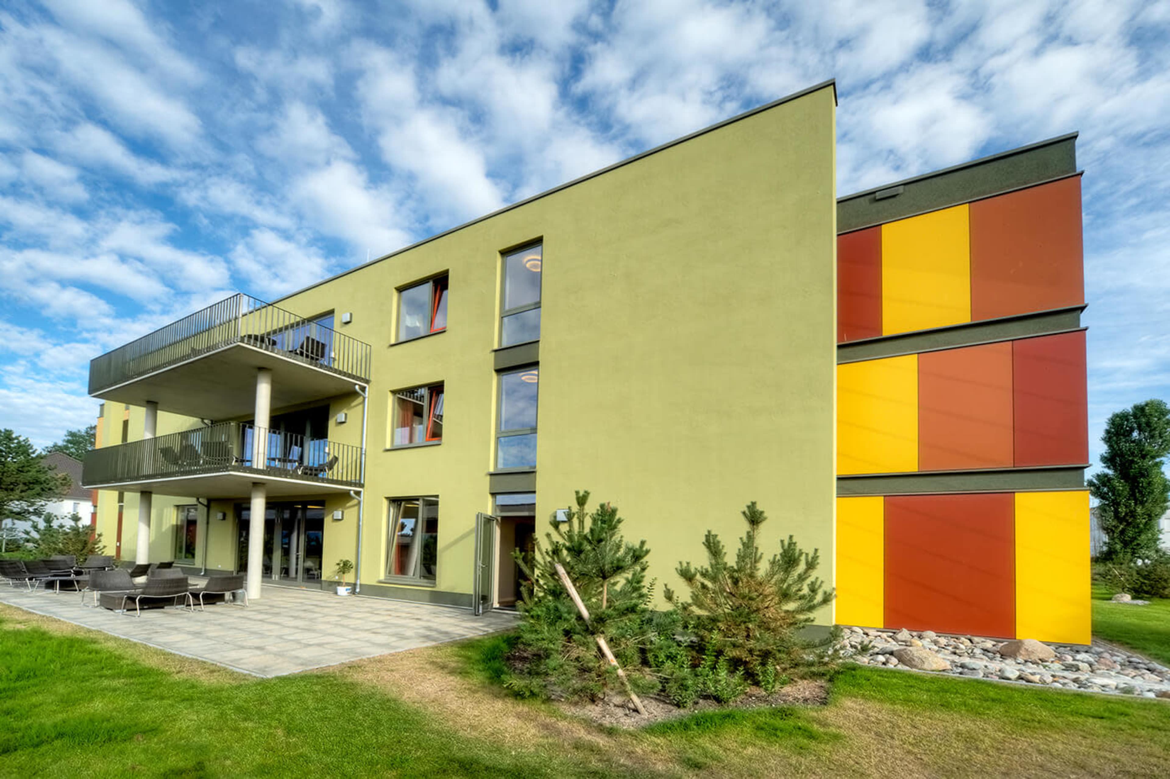 A three-story modern apartment building with a green exterior and colorful orange and yellow accent walls.