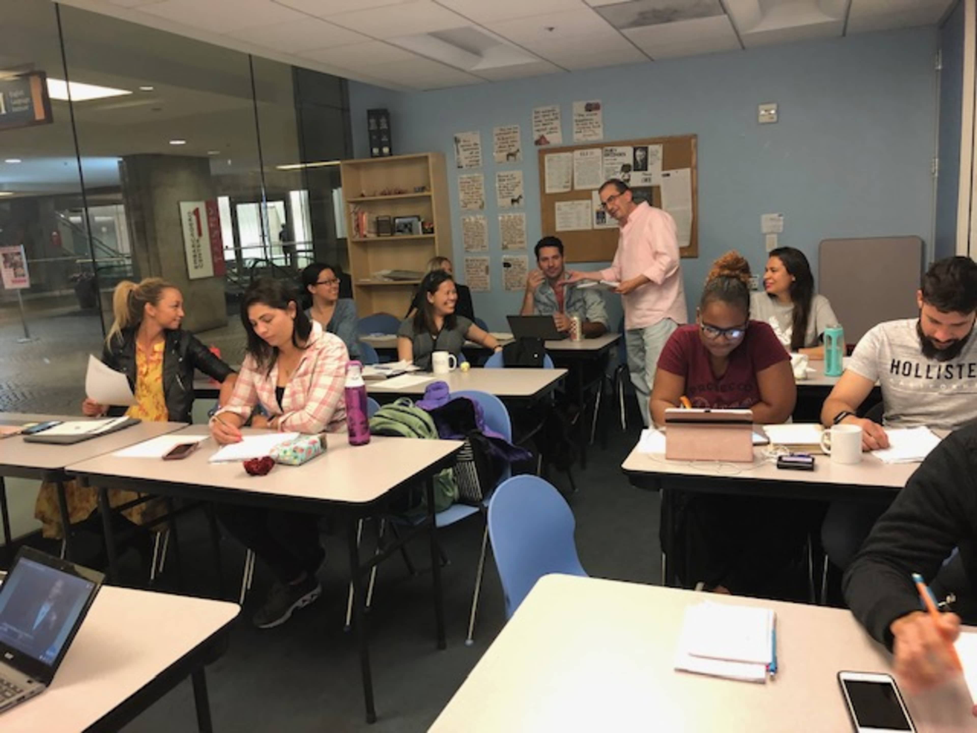 A group of students is engaged in discussion and studying at desks in a classroom setting.
