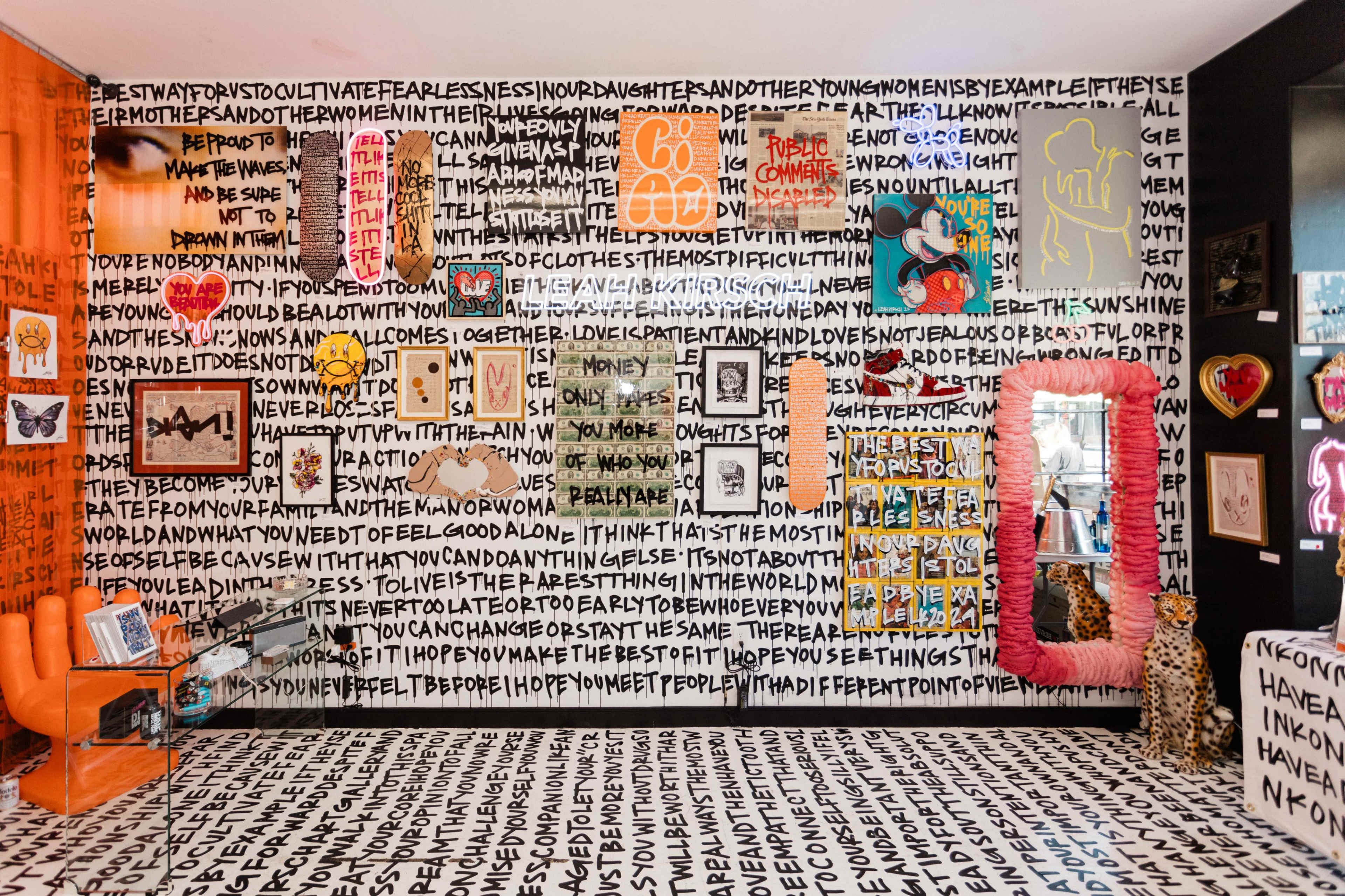 A colorful room with a patterned wall covered in bold, handwritten text and various framed artworks, including photographs and illustrations, arranged along the walls.