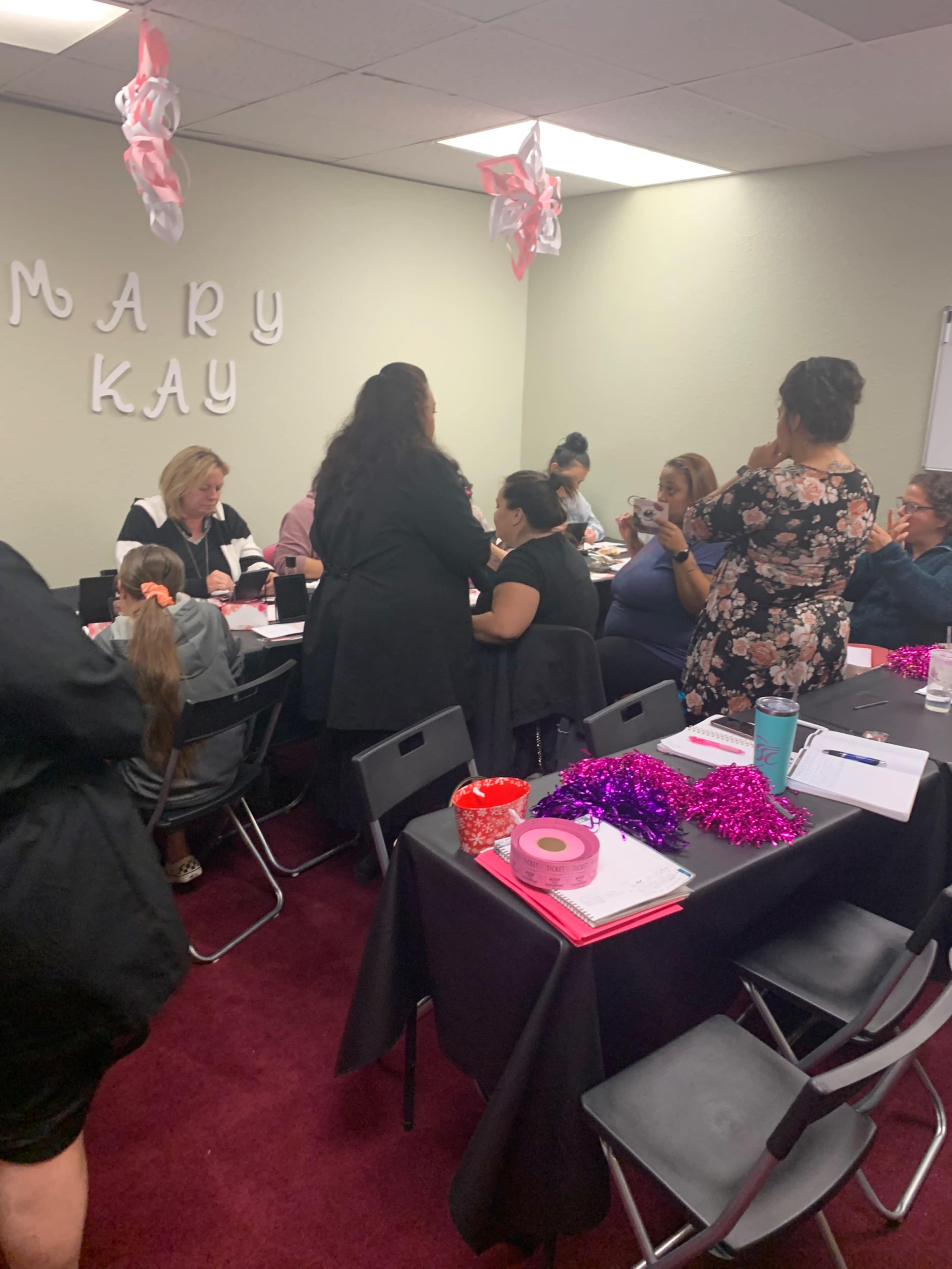 A group of people gathers around tables in a room decorated for a Mary Kay event.