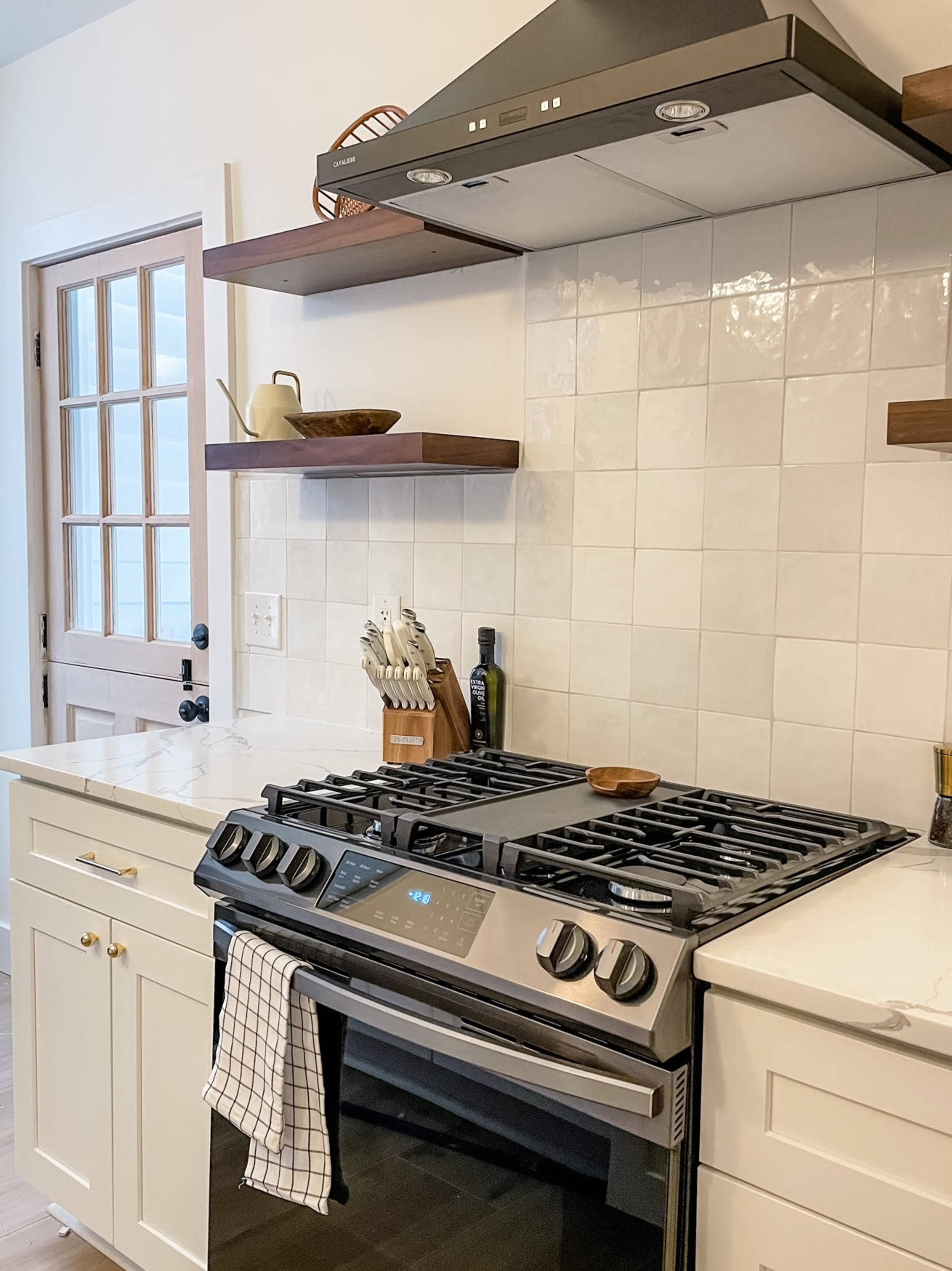 A modern kitchen with a gas stove, hood, and open shelves filled with kitchen utensils and decor.