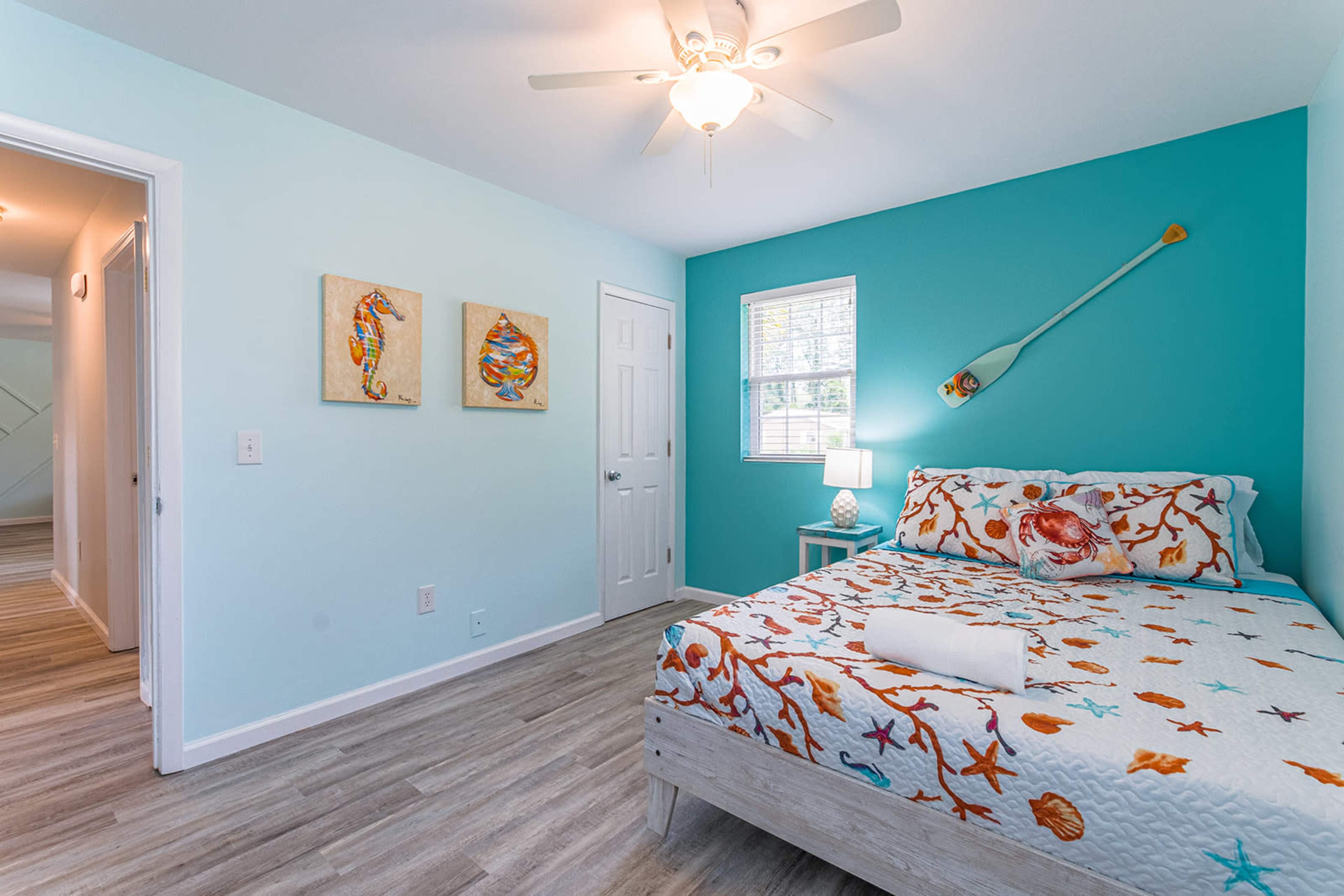 A brightly colored bedroom features a bed with an ocean-themed quilt, light blue walls, and nautical decor.