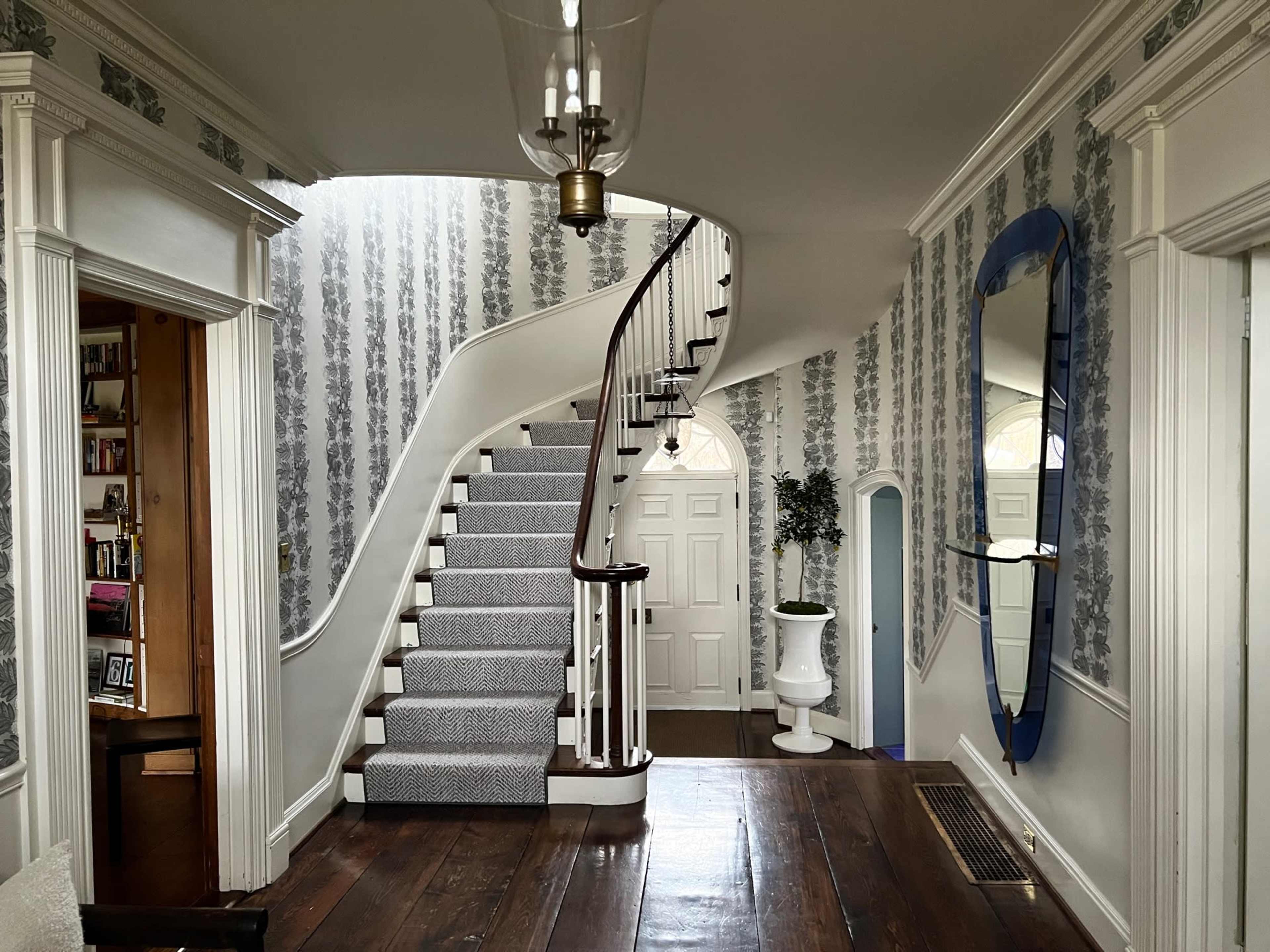 A spacious hallway featuring a spiral staircase, floral wallpaper, and an ornamental mirror.