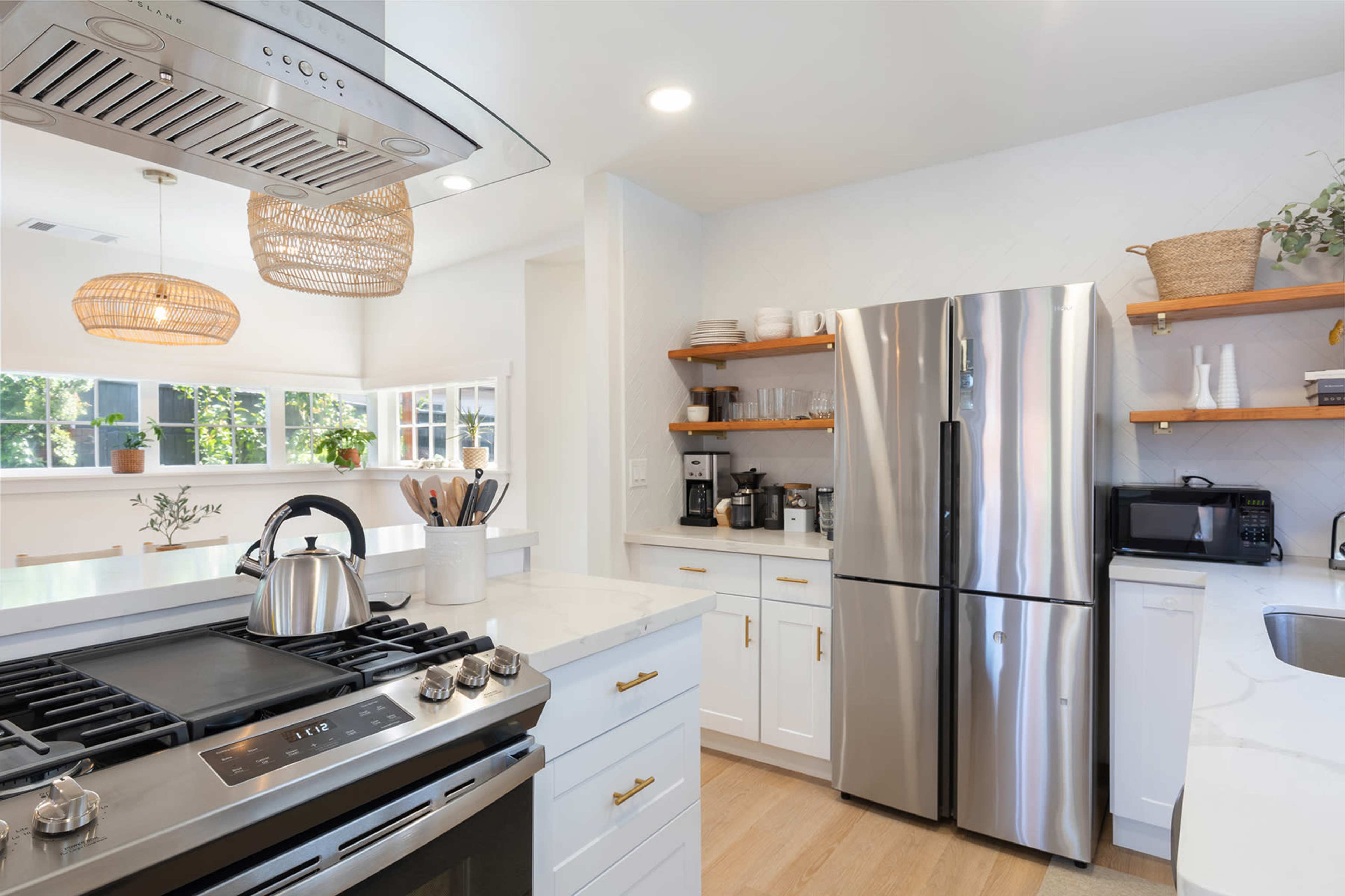 A modern kitchen features stainless steel appliances, white cabinets, and open shelving with decorative items and kitchenware.