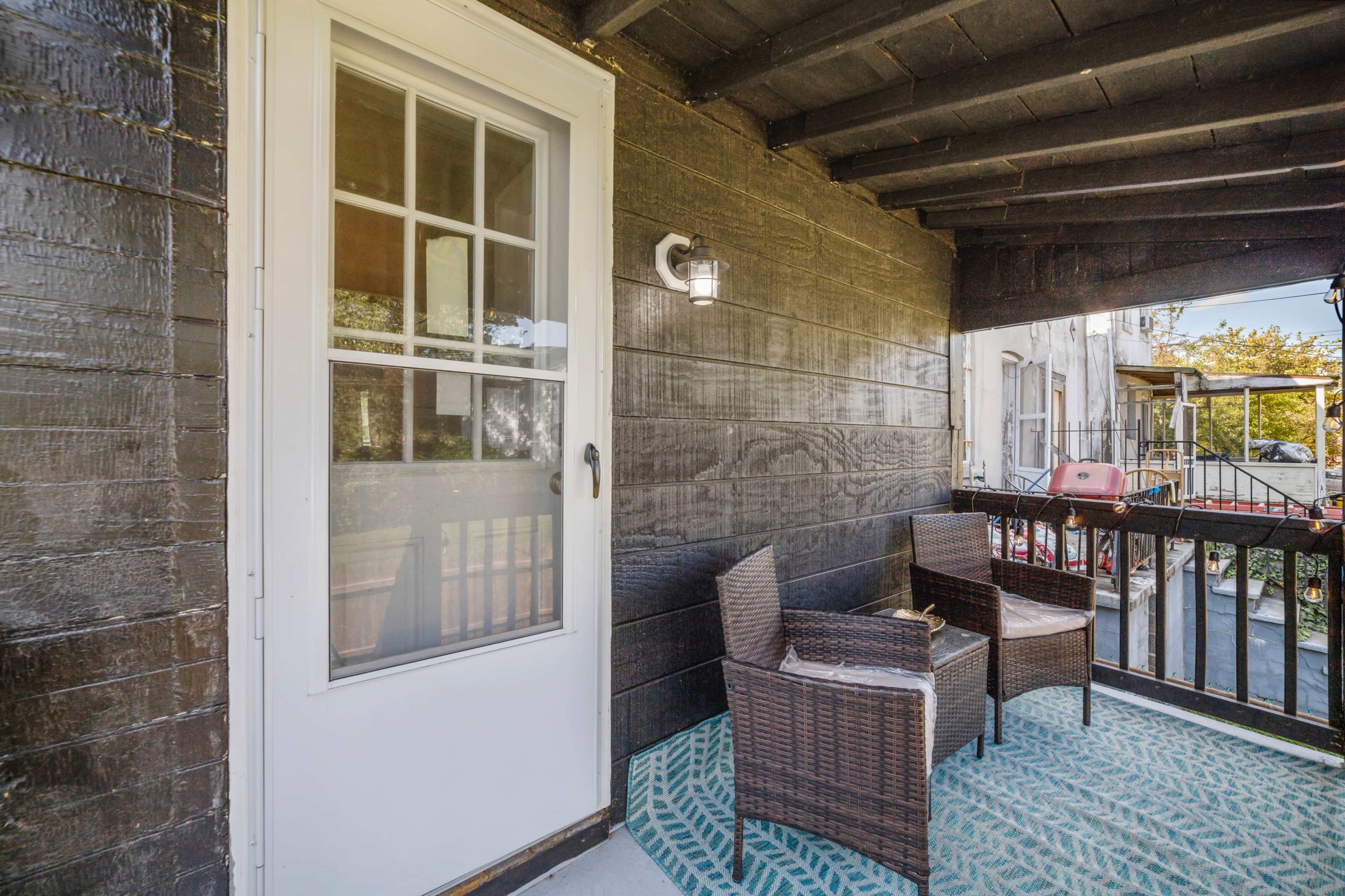 A small balcony features two wicker chairs and a decorative rug in front of a white door.