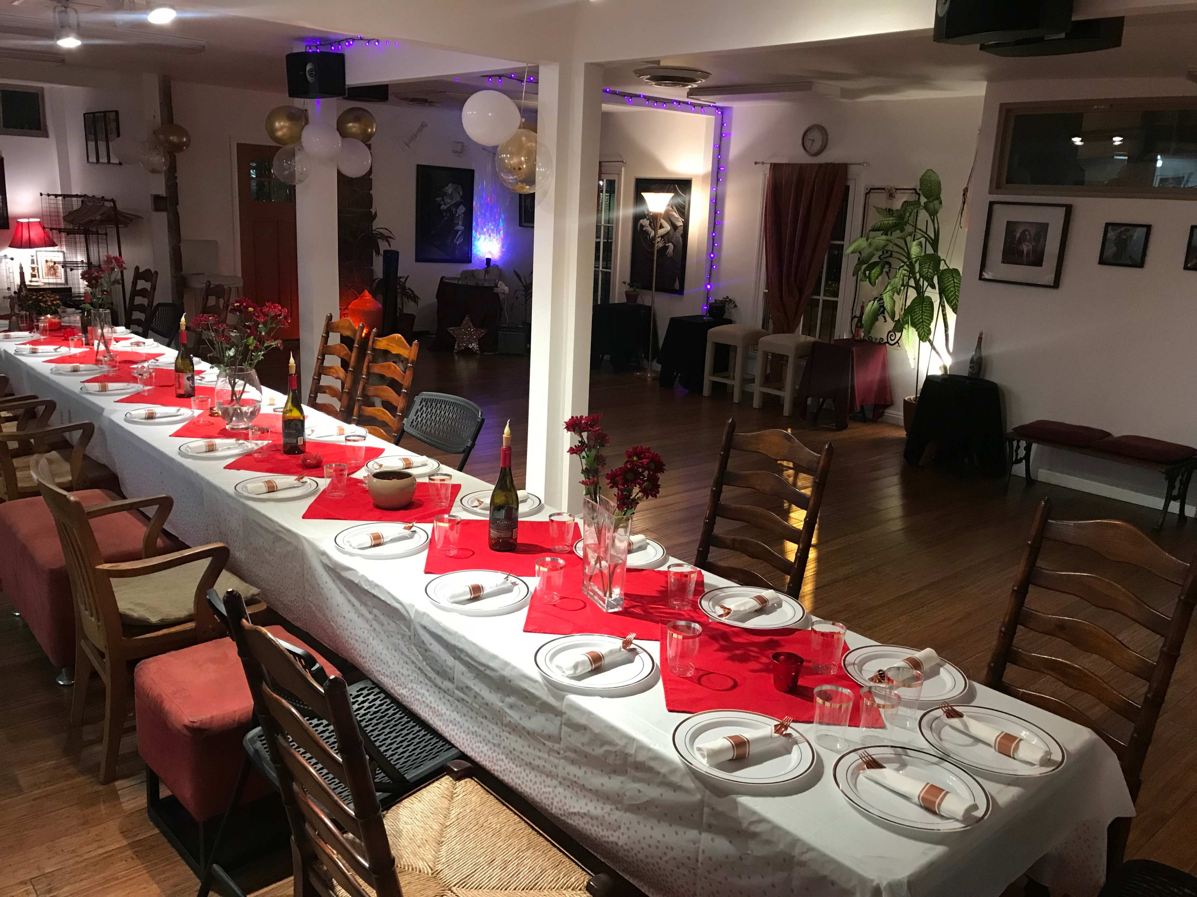 A long dinner table is set with red linens, plates, and centerpieces in a decorated event space.