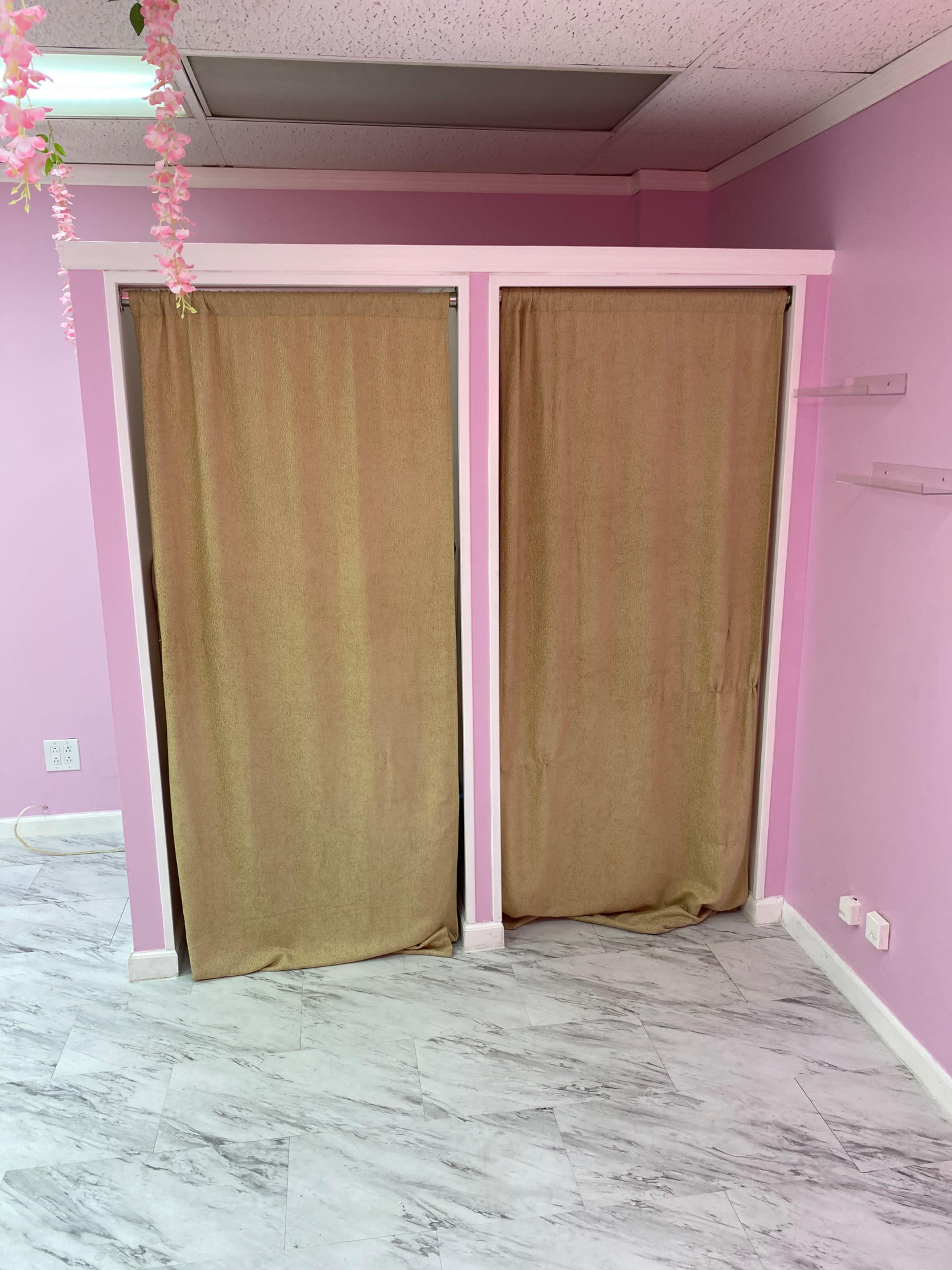 A room with pink walls containing two curtains made of a tan fabric hanging in front of a closet or changing area.