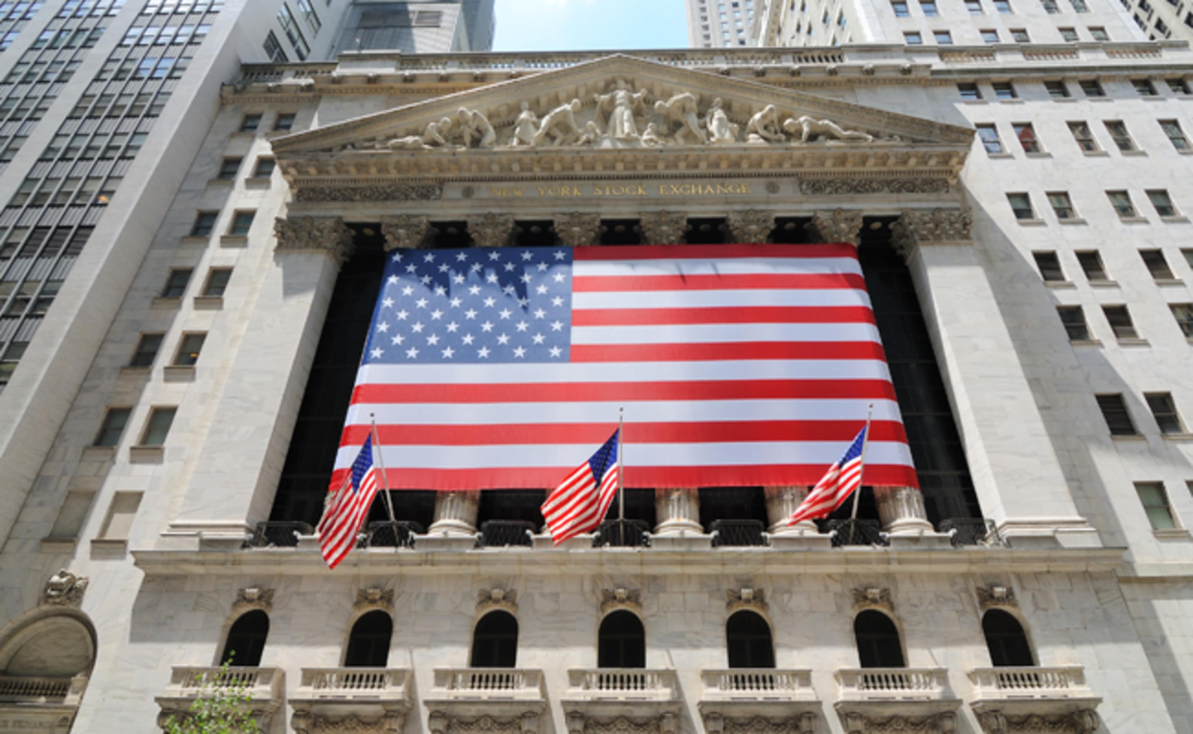 The New York Stock Exchange building displays a large American flag and features several smaller flags at its entrance.
