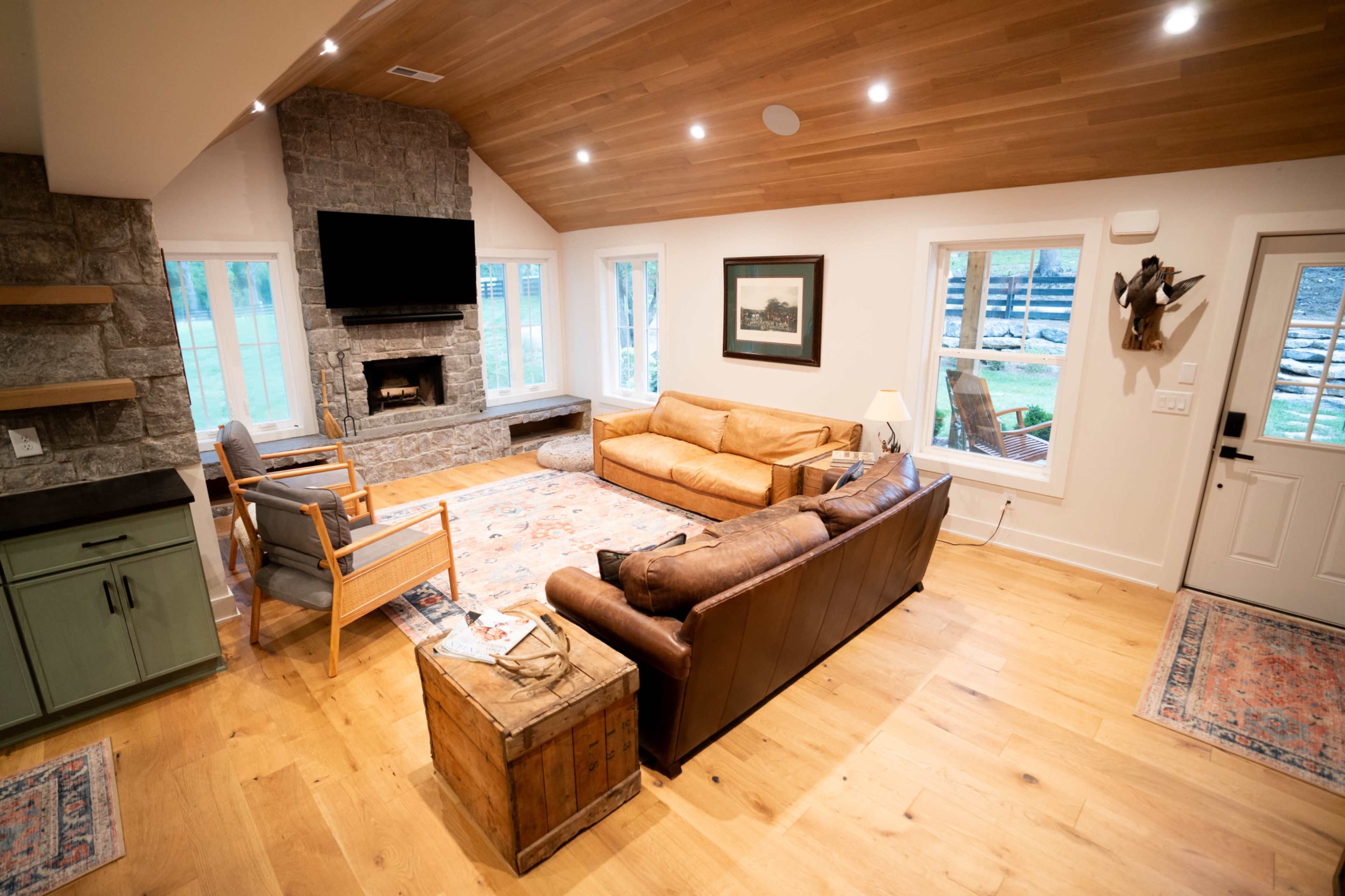 The living room features a stone fireplace, a flat-screen TV mounted on the wall, and a mix of seating options, including two sofas and a pair of chairs.
