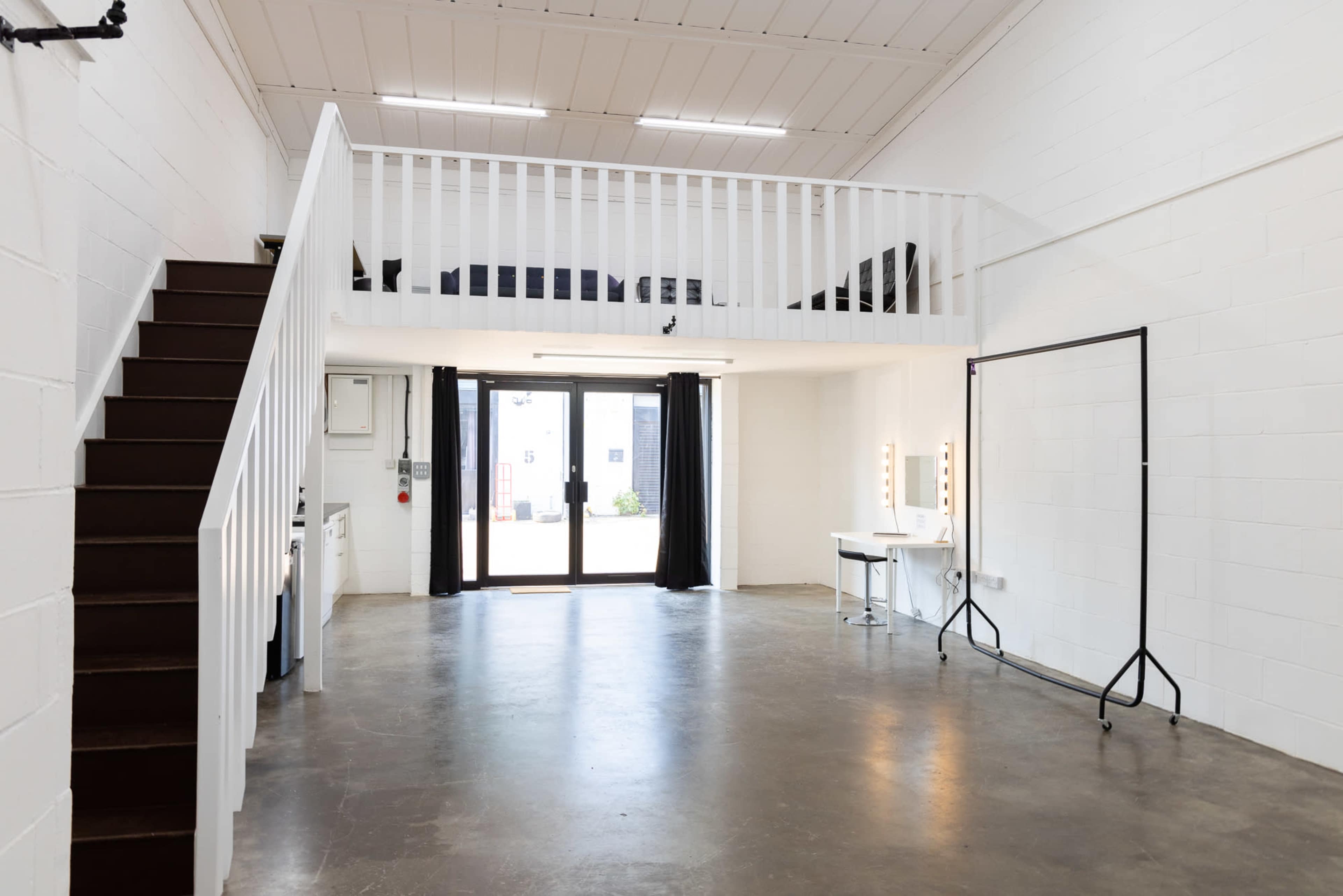 An open interior space with a loft area, a staircase, and a large glass door leading outside.