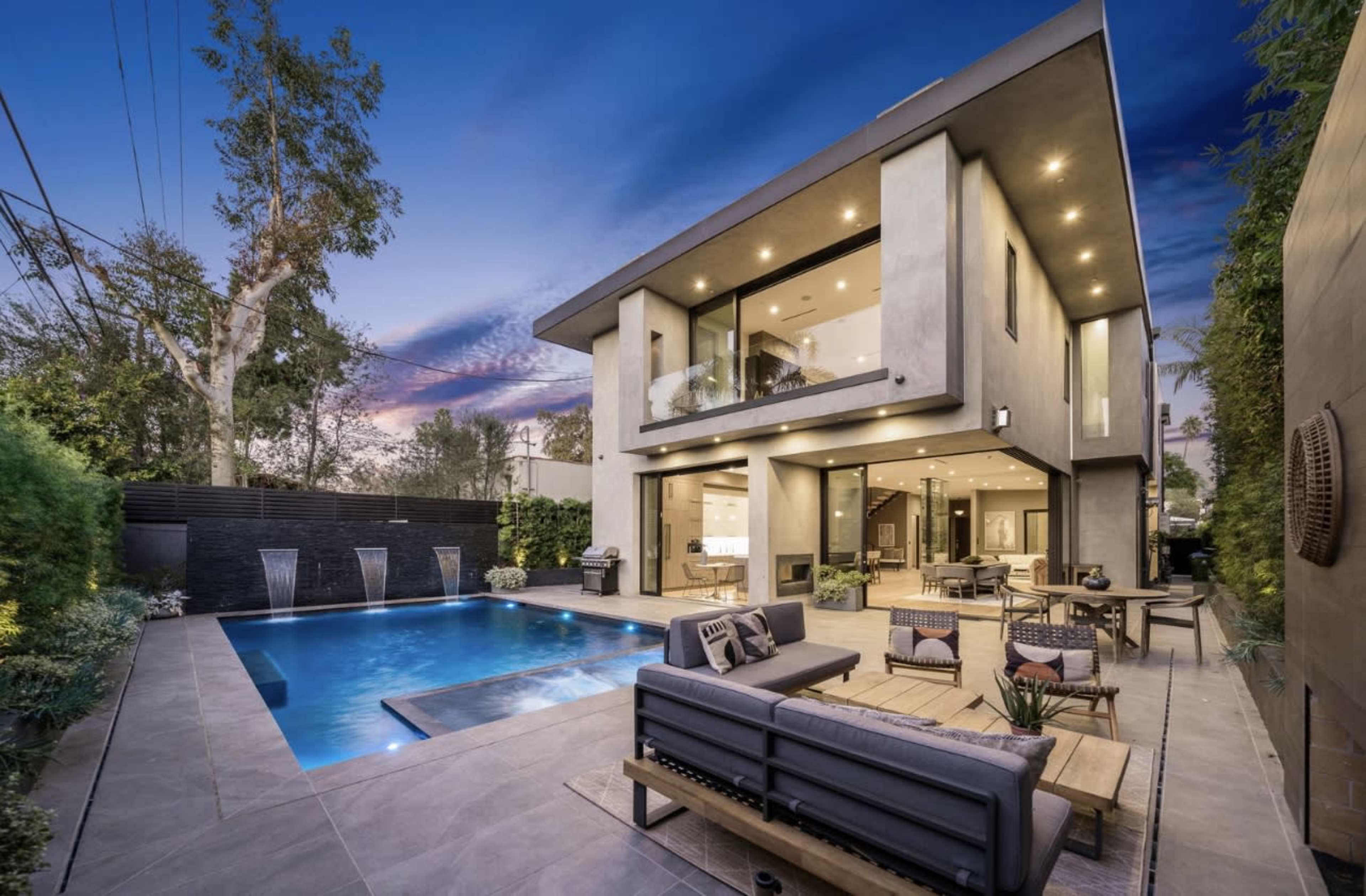 A modern two-story house with large windows and a swimming pool surrounded by a landscaped outdoor area.