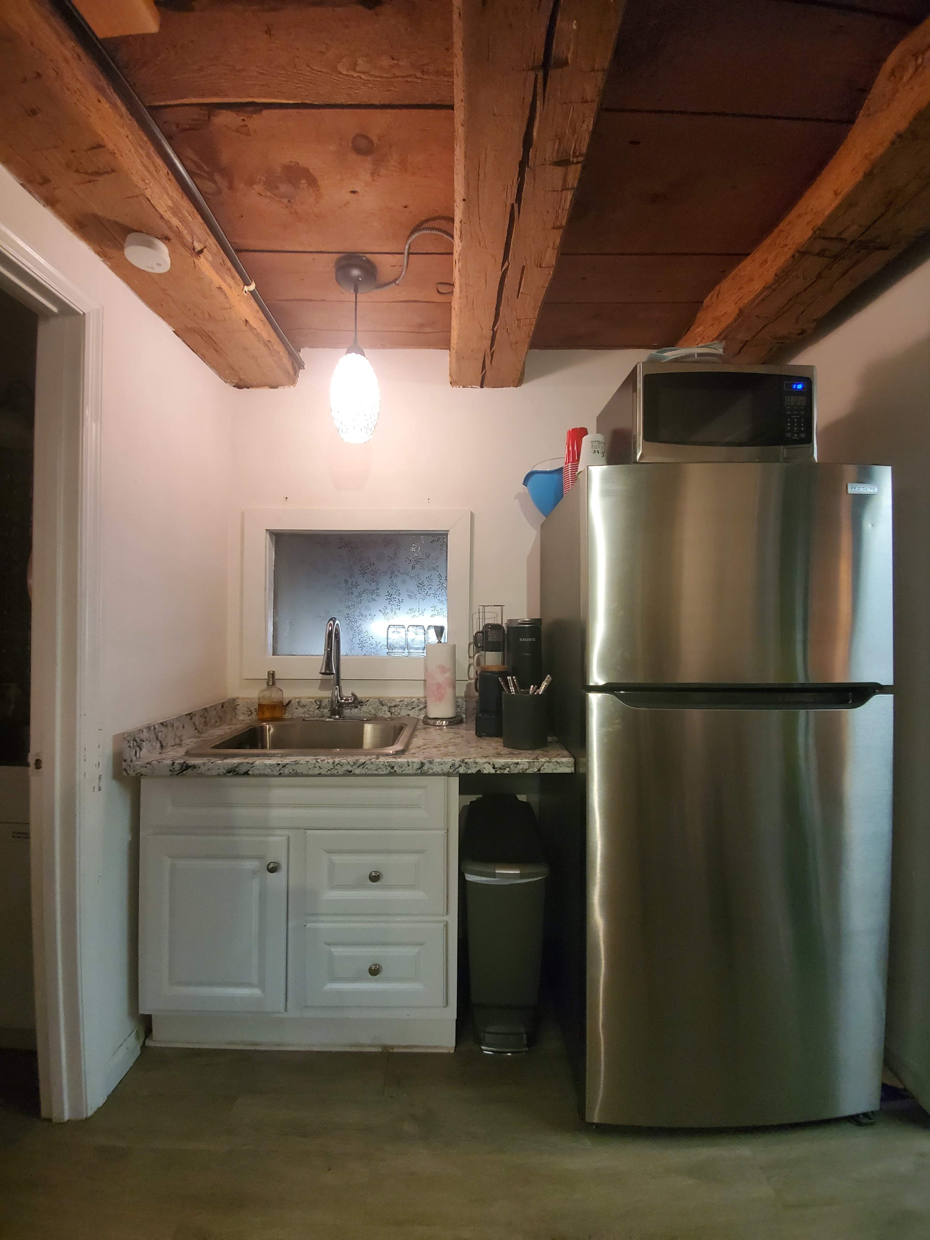 A compact kitchen area featuring a stainless steel refrigerator, a sink with a granite countertop, and wood beams on the ceiling.