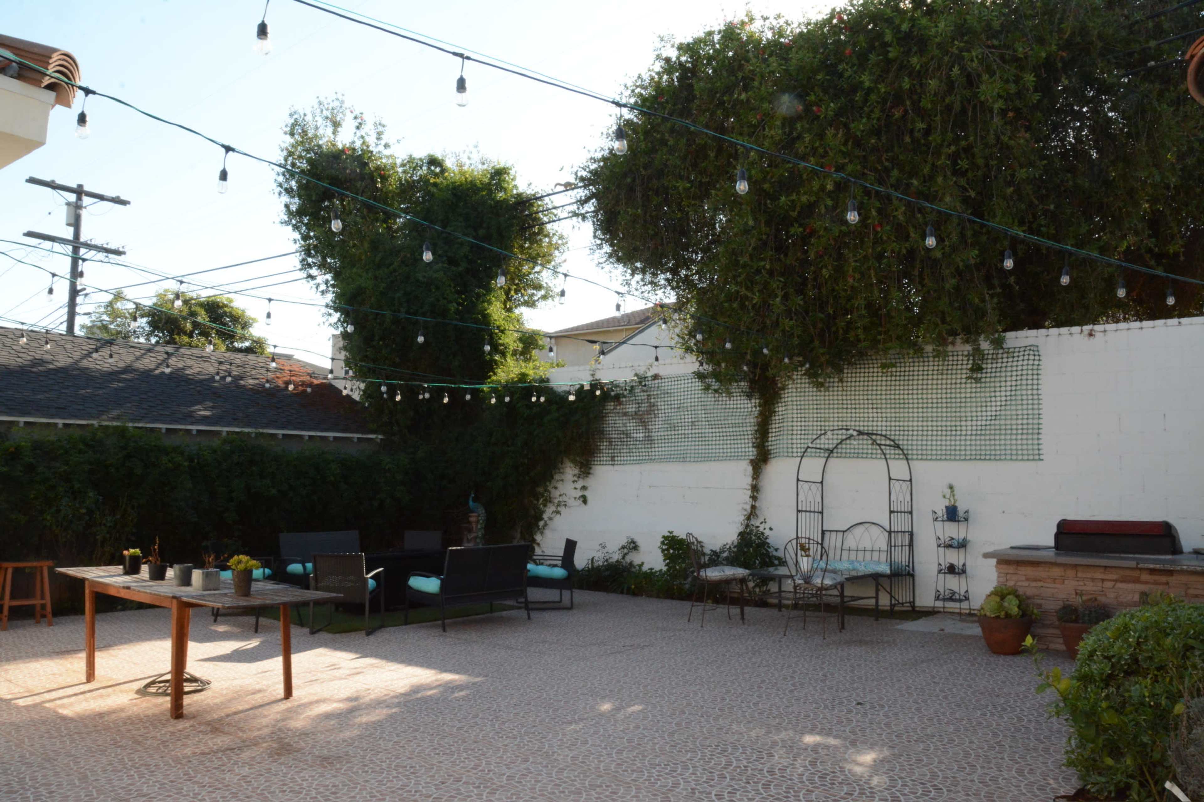 A patio area with string lights overhead, seating arrangements, and a brick wall covered with greenery.