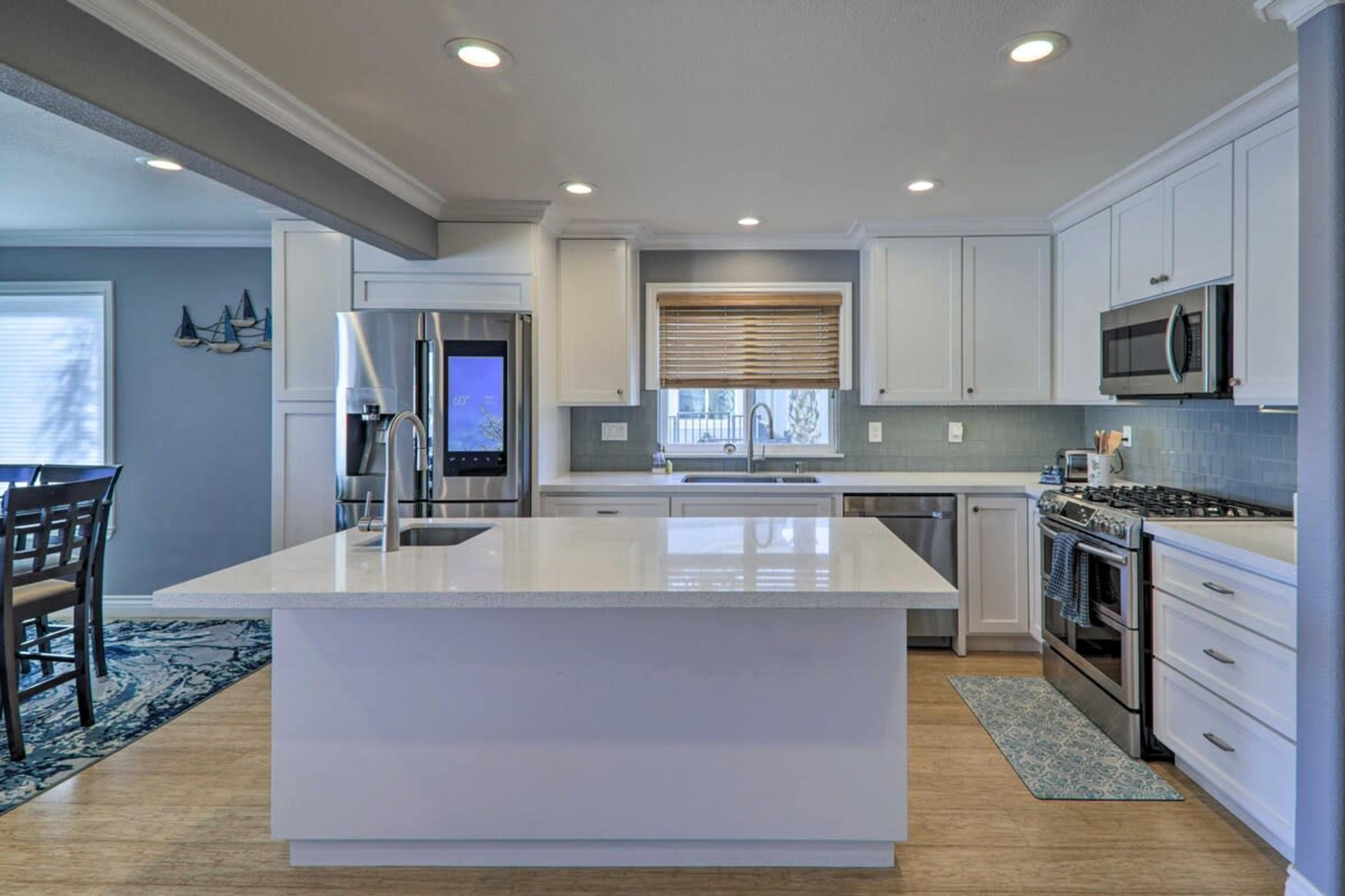 A modern kitchen features white cabinetry, stainless steel appliances, and a large central island with a light countertop.