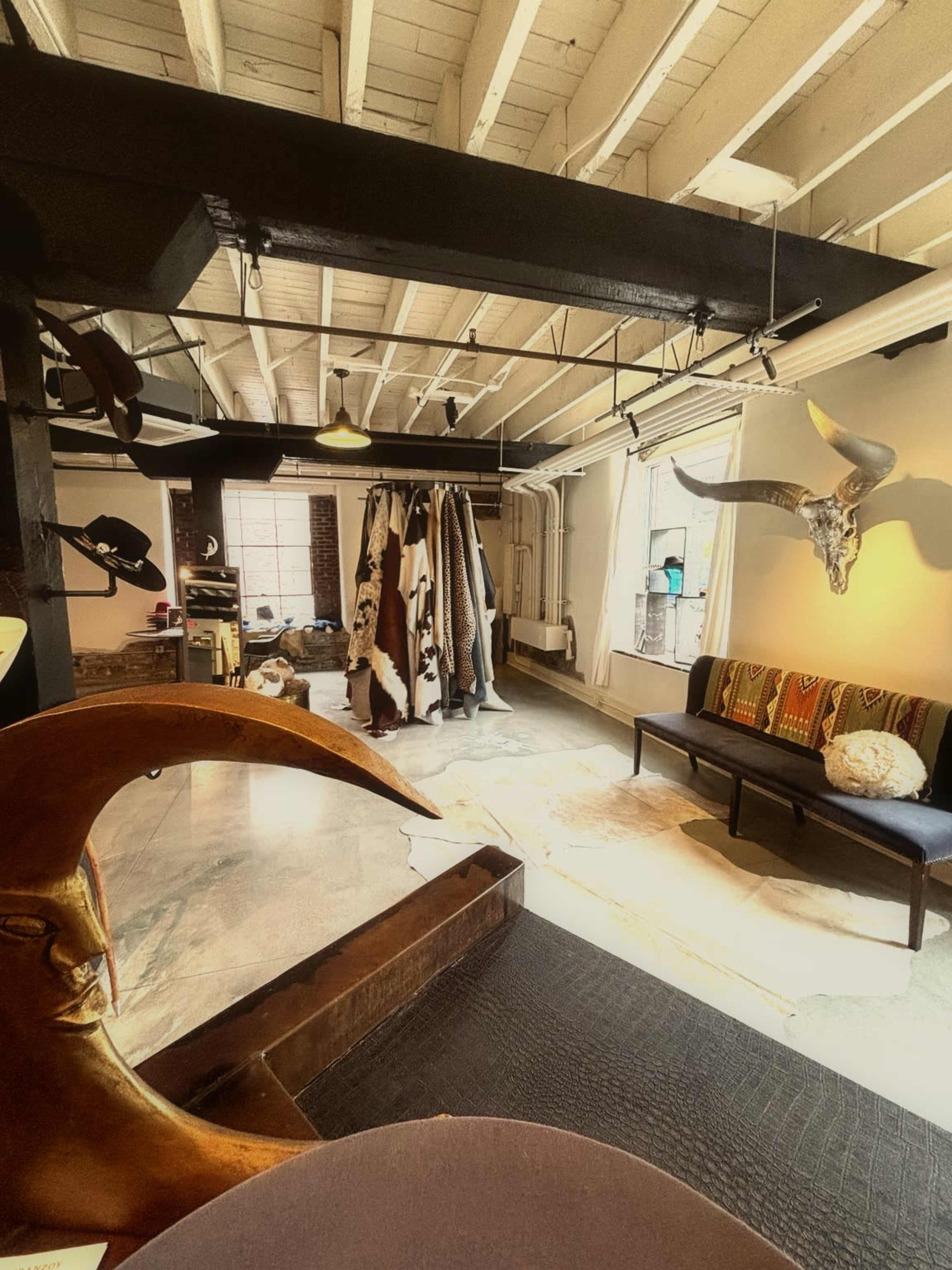 The image shows a spacious room with exposed beams, featuring clothing racks, a decorative sofa with patterned cushions, and a large decorative moon sculpture in the foreground.