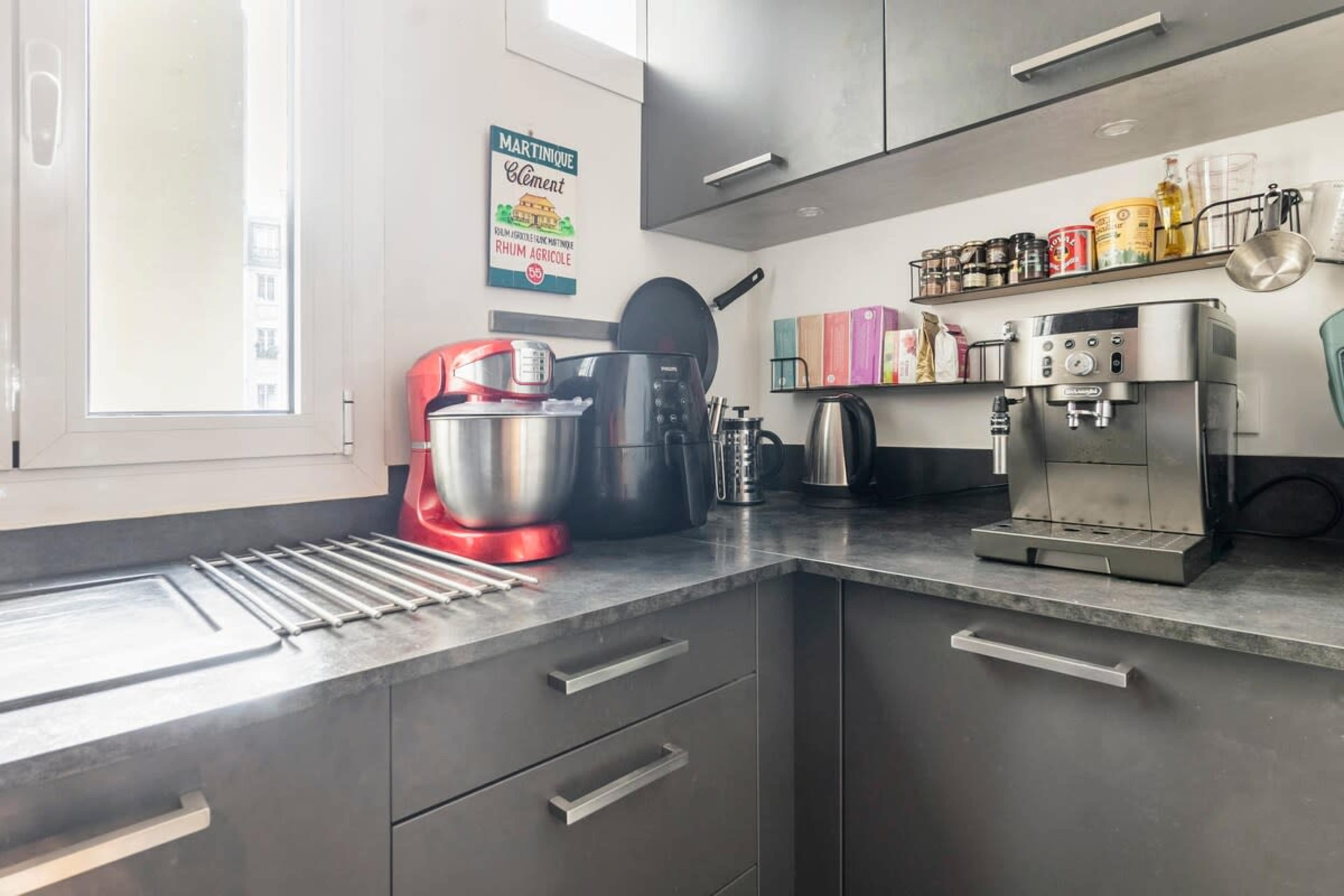 A modern kitchen with gray cabinets, a countertop featuring a stand mixer, an espresso machine, and various kitchenware arranged neatly.