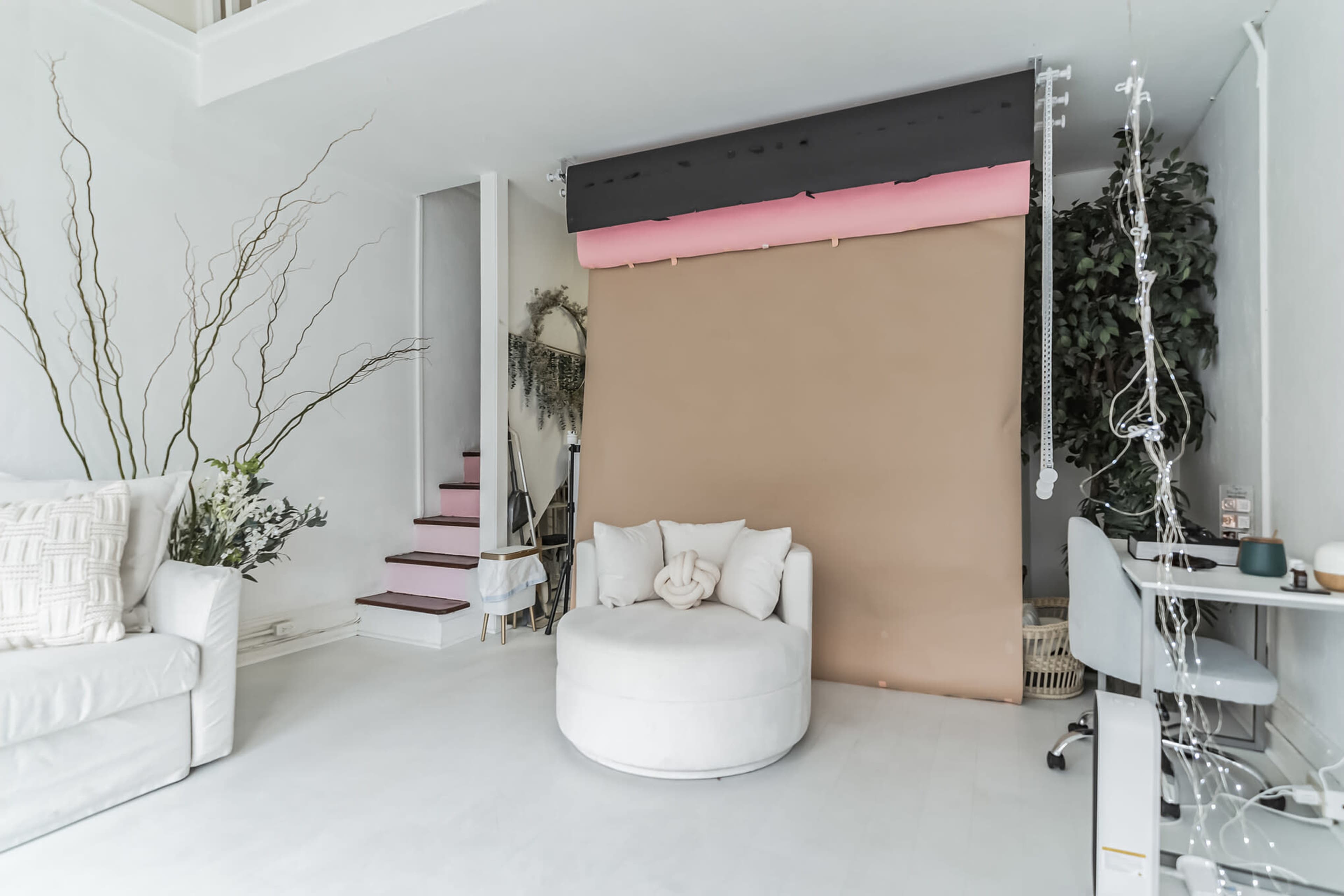 A spacious interior features a white couch, a circular chair, and a brown backdrop with a staircase and plants in the background.
