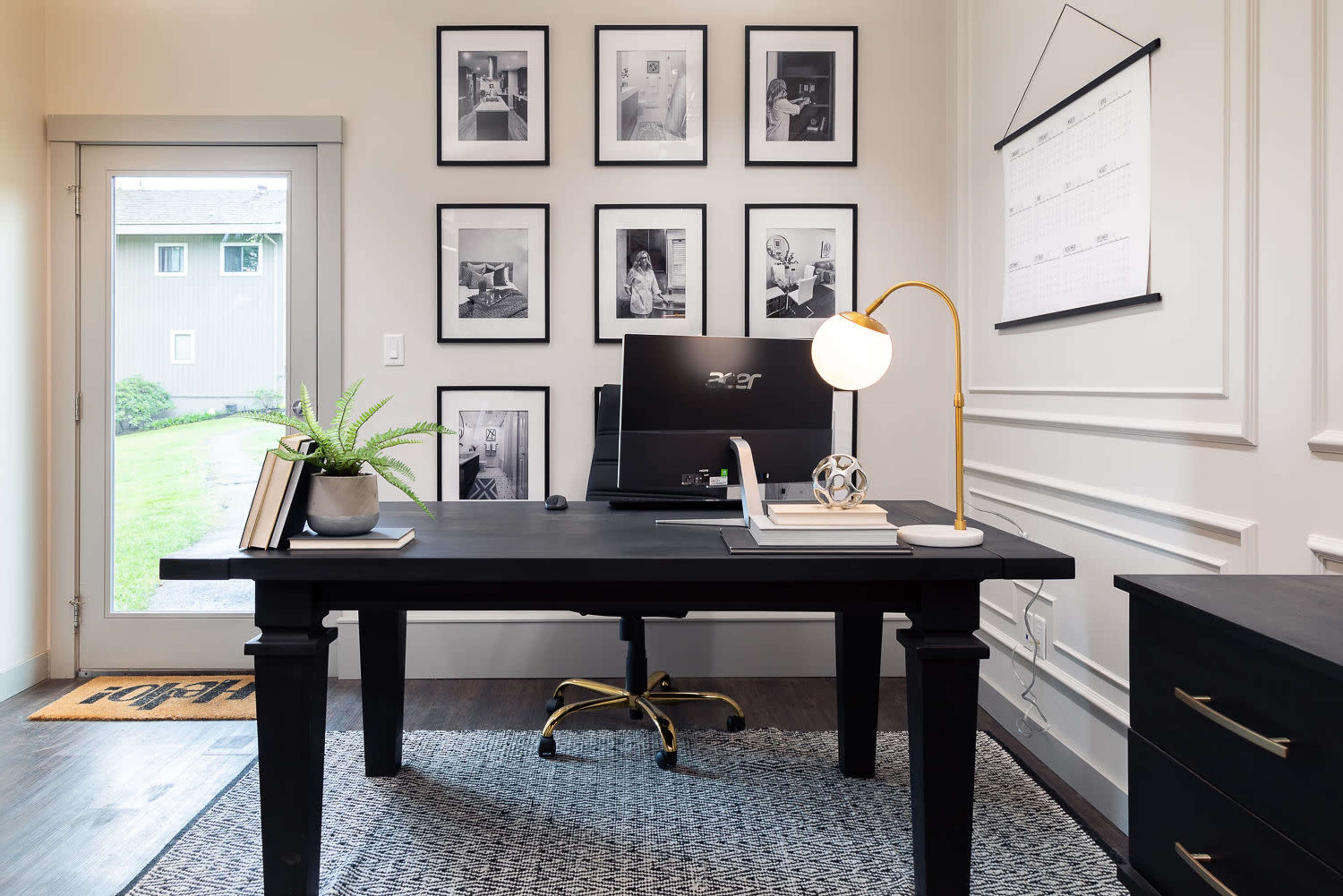 A modern home office with a black desk, an ergonomic chair, a computer on the desk, and several framed black-and-white photographs hanging on the wall.