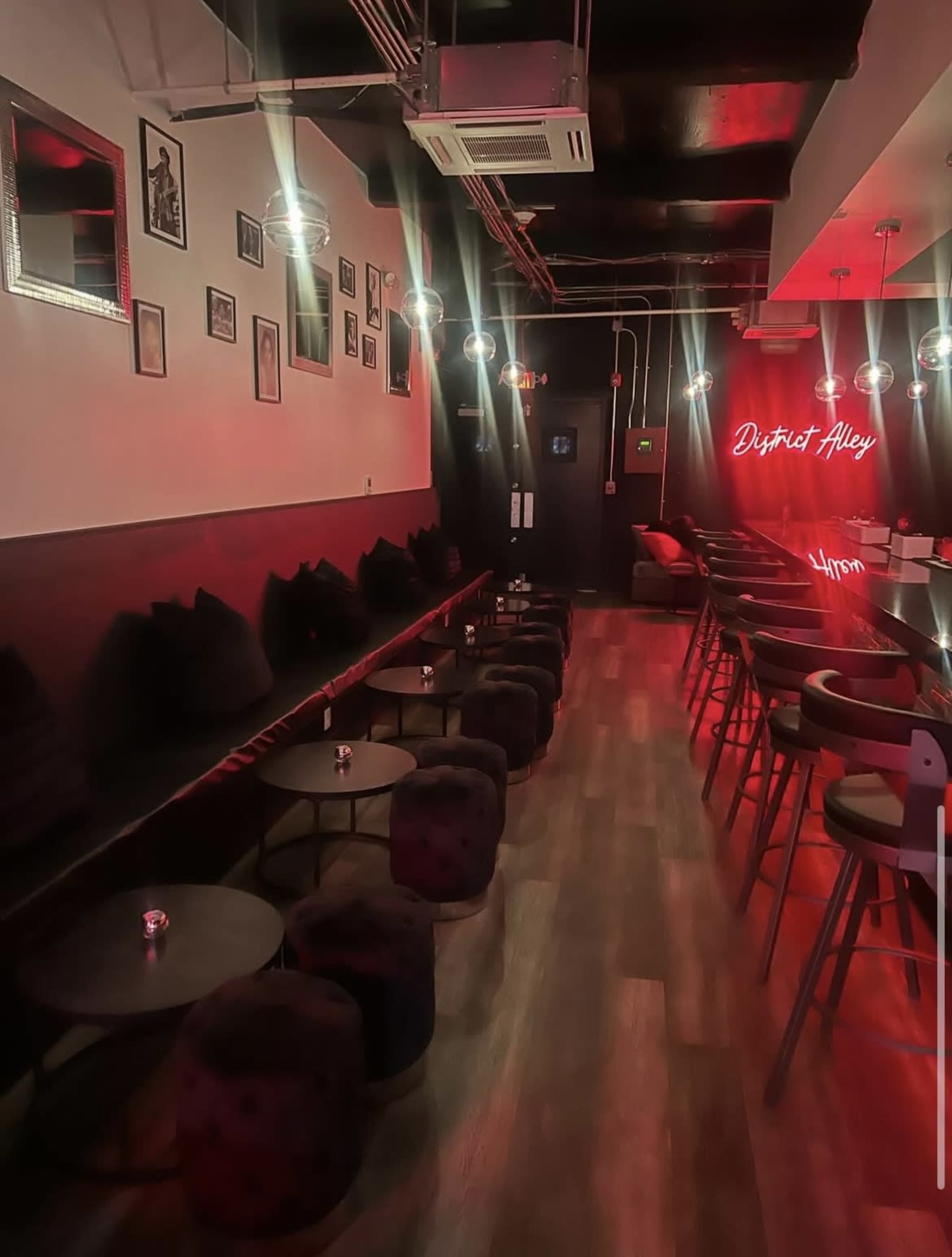 The image shows a dimly lit lounge with plush seating, small tables, and a neon sign that reads "Dysthet Alley."