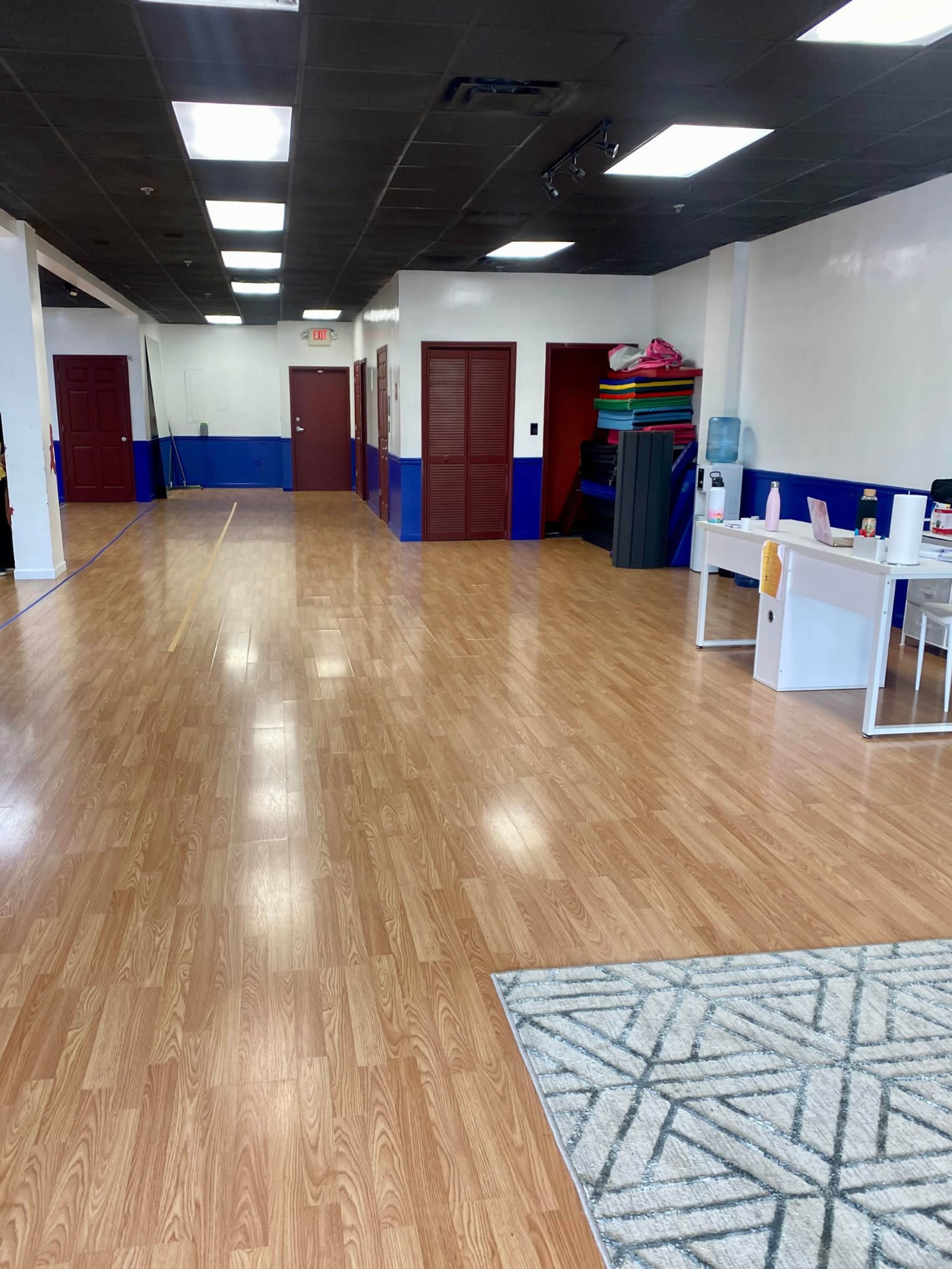 A spacious, brightly lit interior with wooden flooring, featuring several closed doors and a reception area with a desk and water cooler.