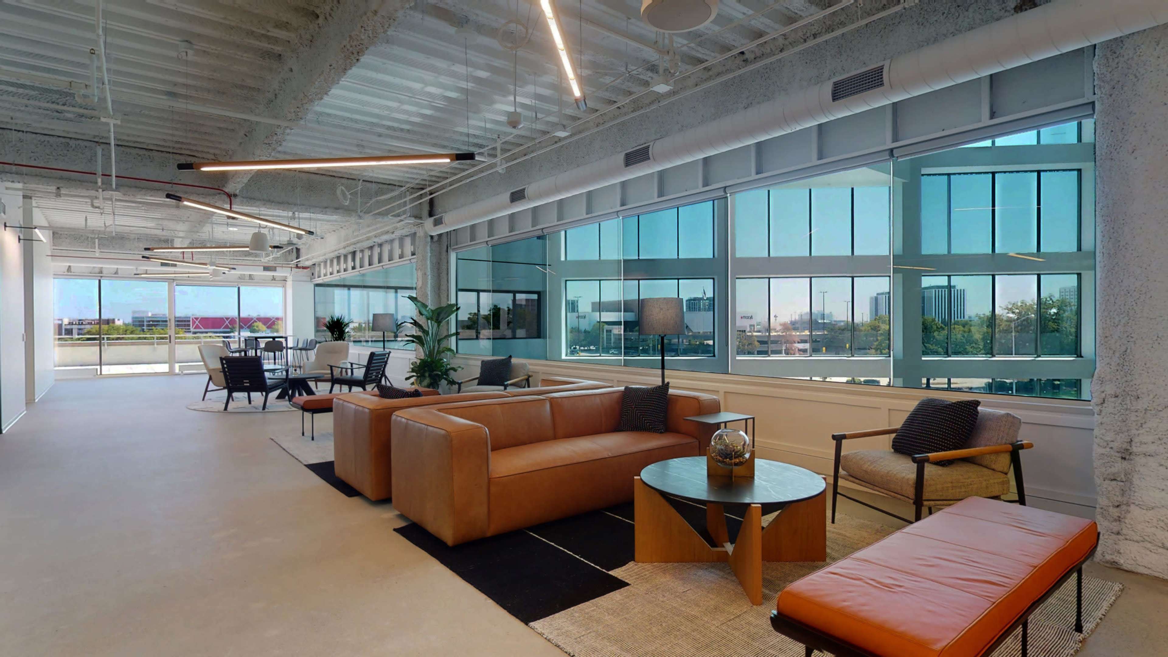 A modern office space featuring large windows with natural light, brown leather seating, and a minimalistic design.