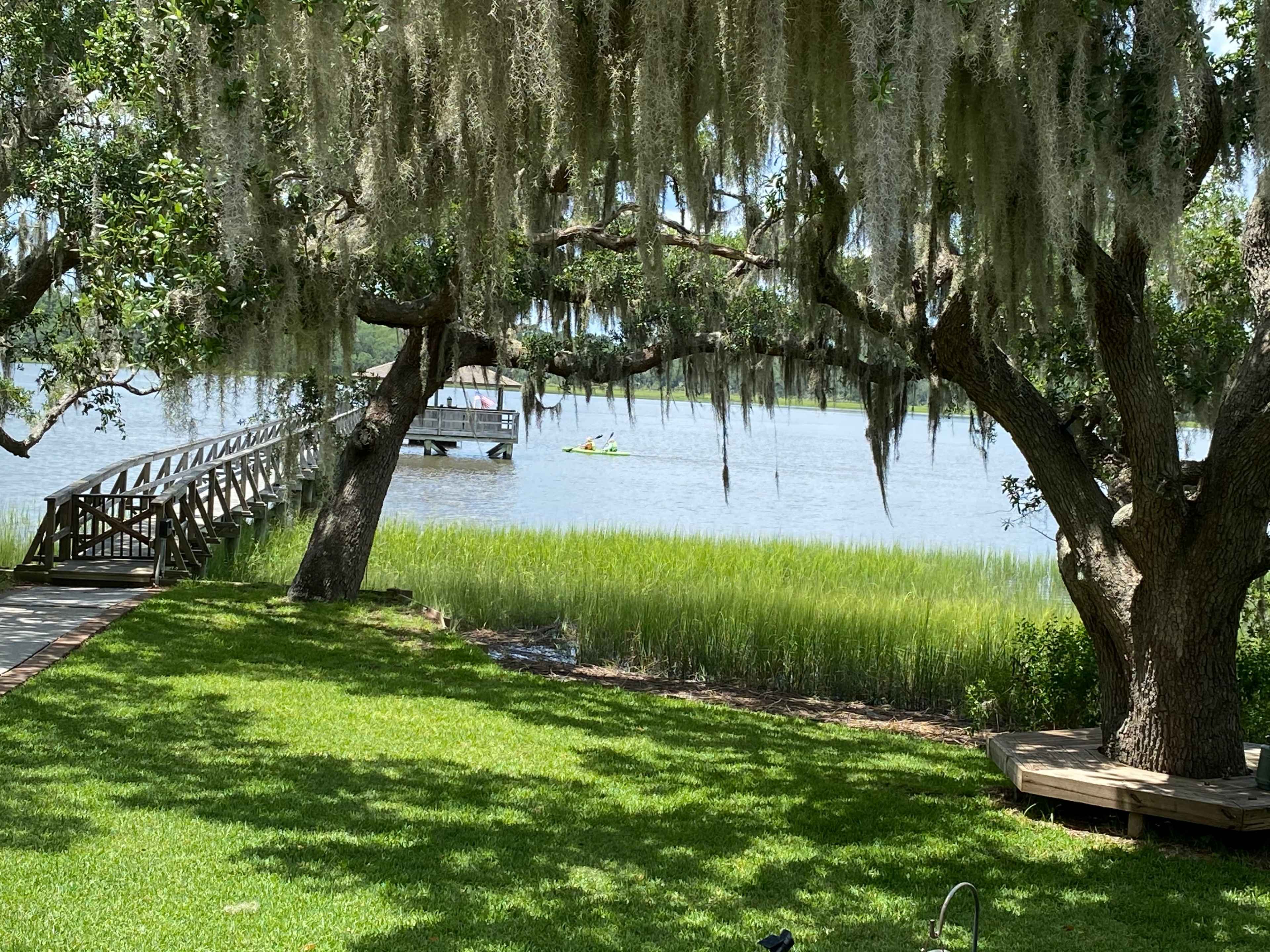 A wooden dock extends over the water, framed by trees draped with Spanish moss, while two kayakers paddle in the distance.