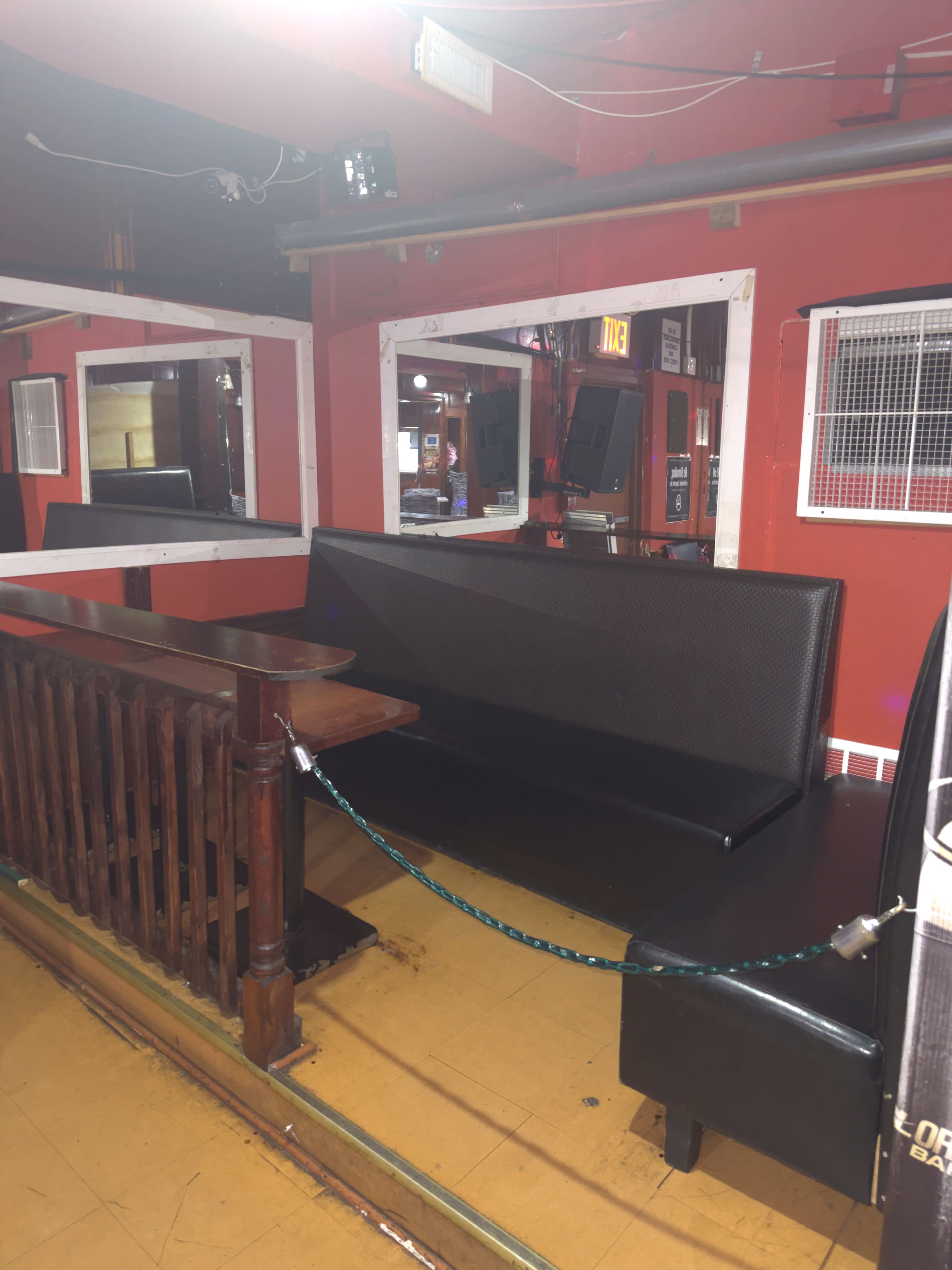 A section of a bar with a black leather bench, a wooden railing, and mirrors on the walls, all against a red background.