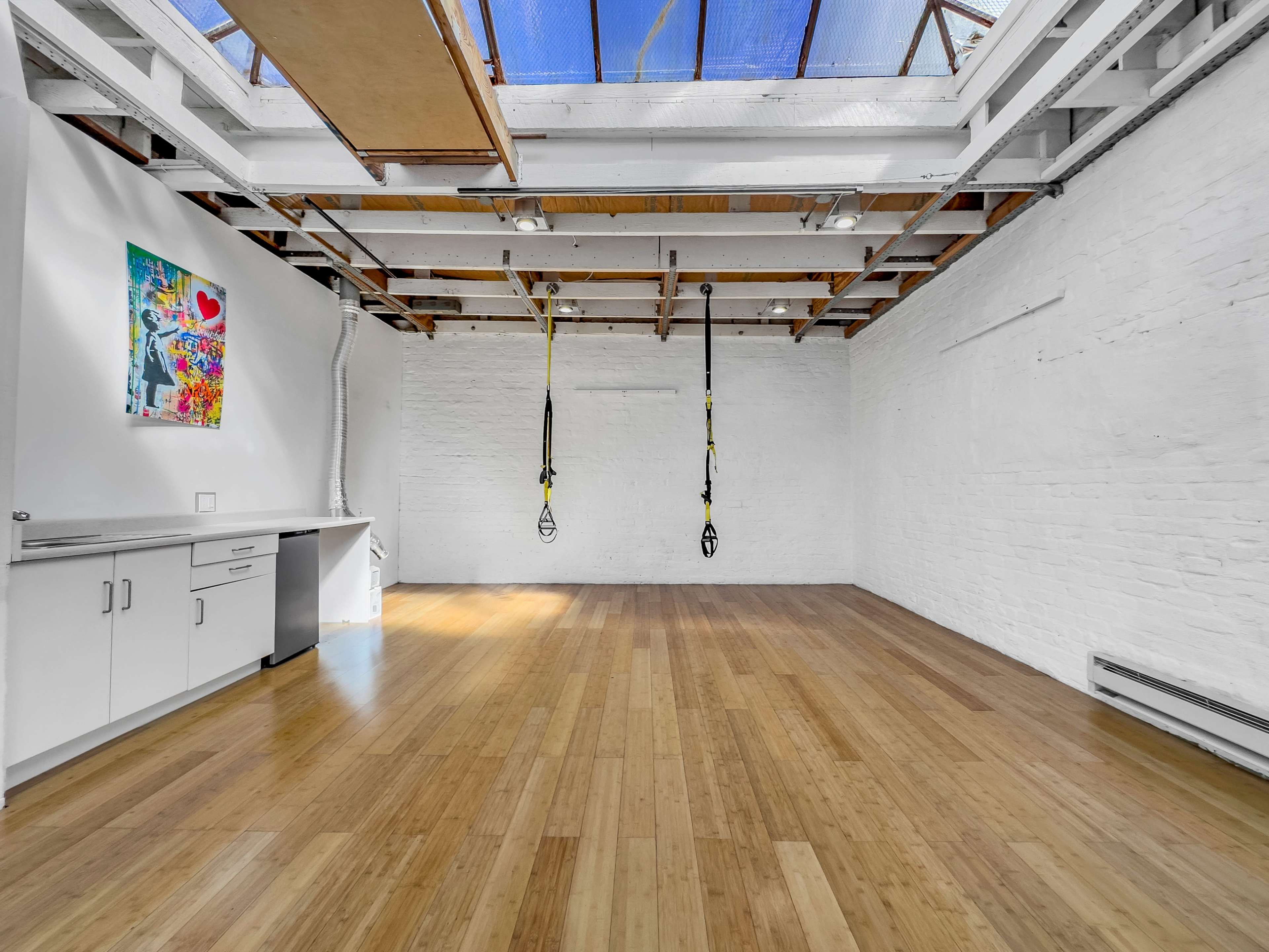 A spacious, bright room with bamboo flooring, white brick walls, and yellow suspension straps hanging from the ceiling.