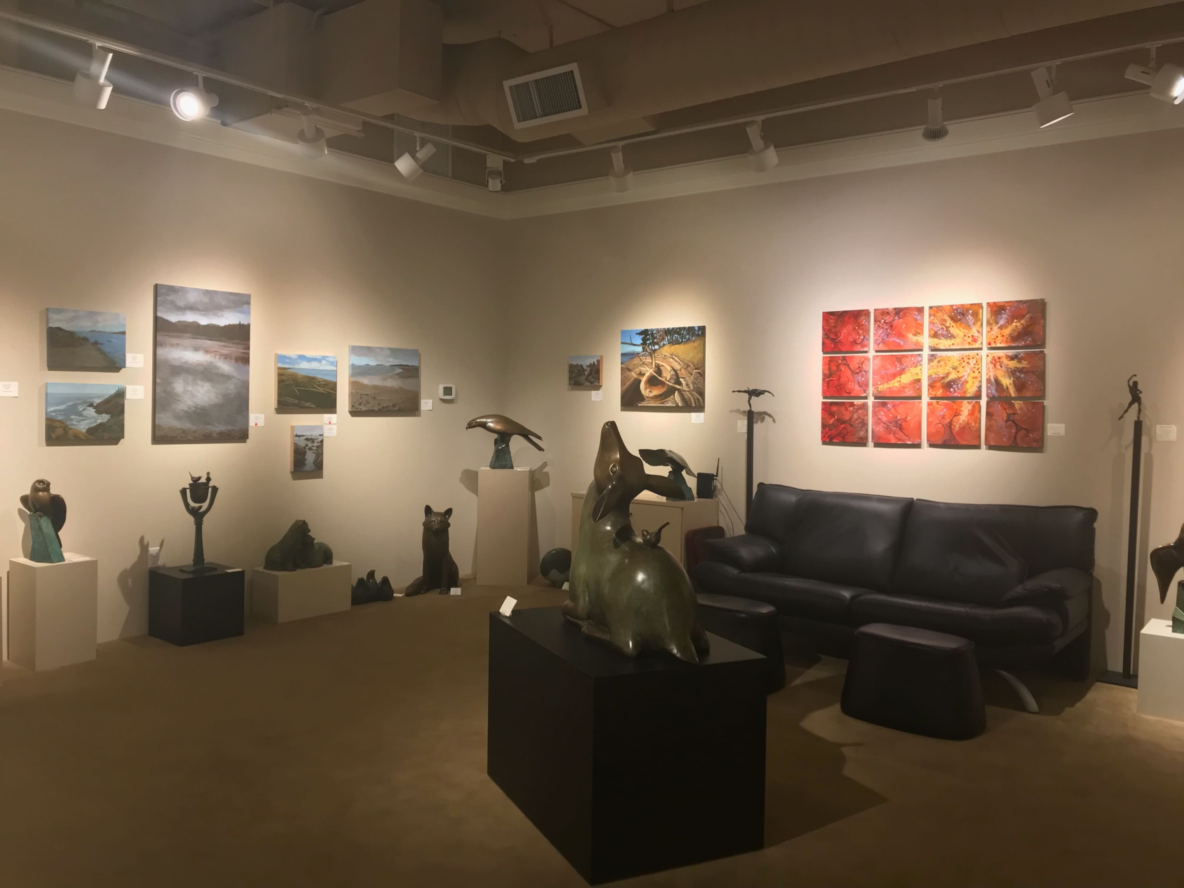 An art gallery featuring various paintings and sculptures, with a leather couch positioned near the artwork on display.