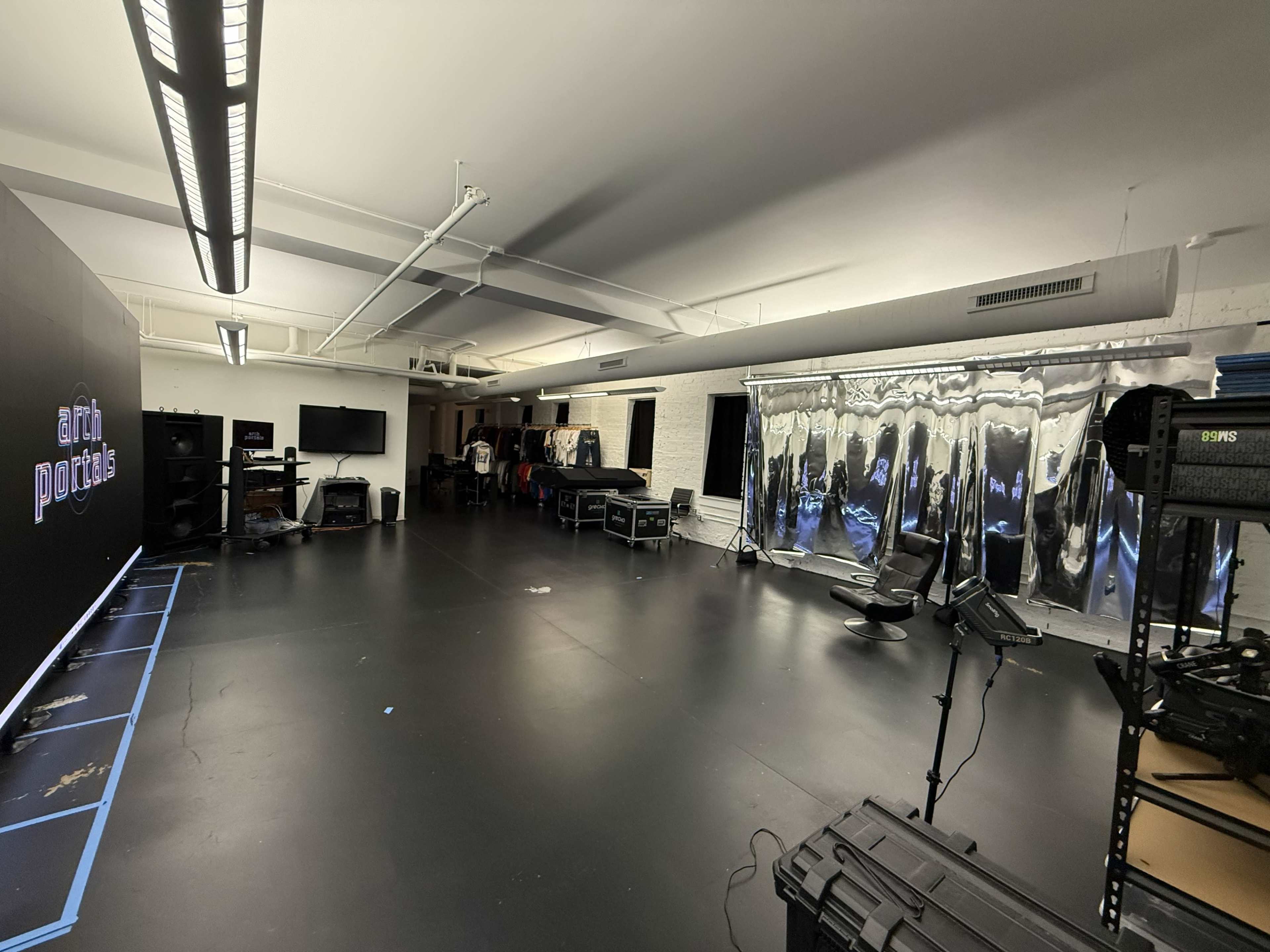 The image shows a spacious studio with a polished black floor, equipment racks, and a large reflective backdrop on one wall.