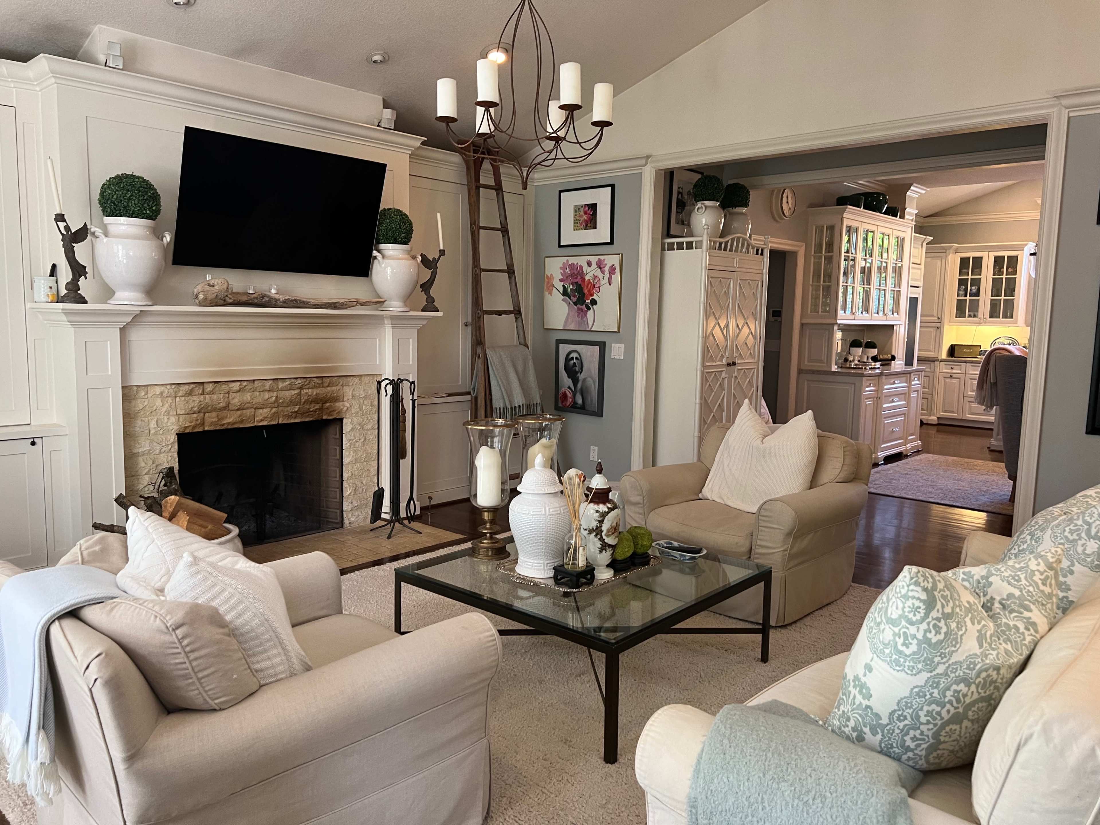 A cozy living room features two armchairs facing a glass coffee table, a fireplace with a stone surround, and a large television mounted on the wall.